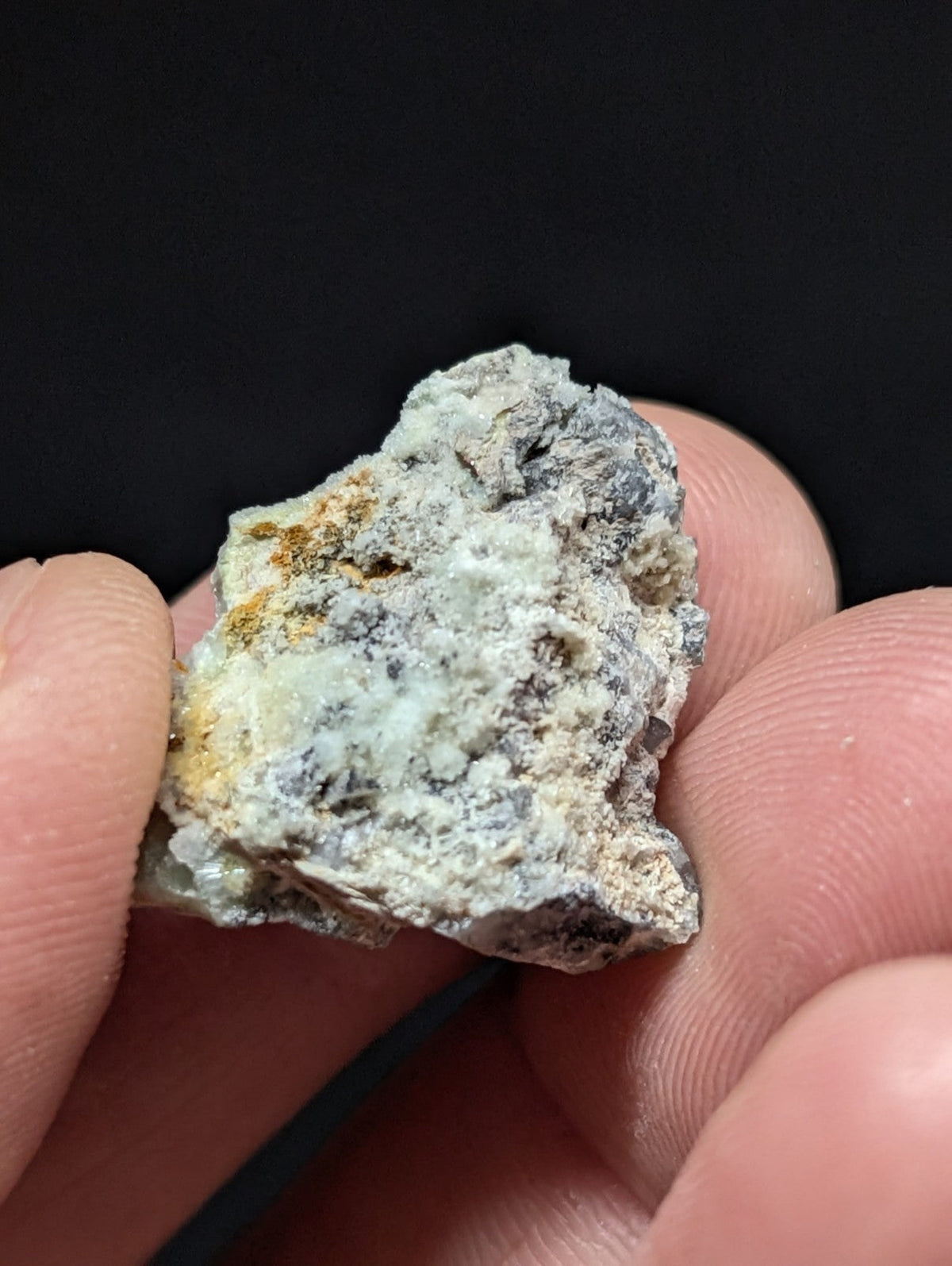 A rough, irregularly shaped mineral specimen with a mottled surface of gray, white, and patches of yellowish-orange.
