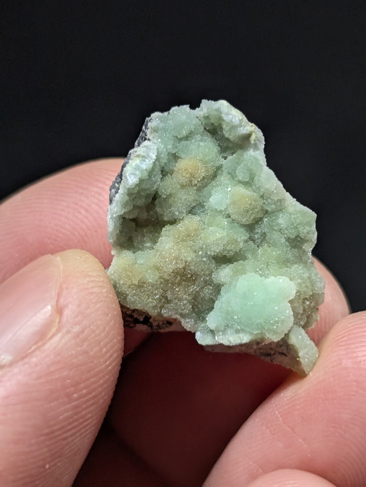 A pale green, crystalline mineral specimen with a rough, textured surface and small yellowish nodules.