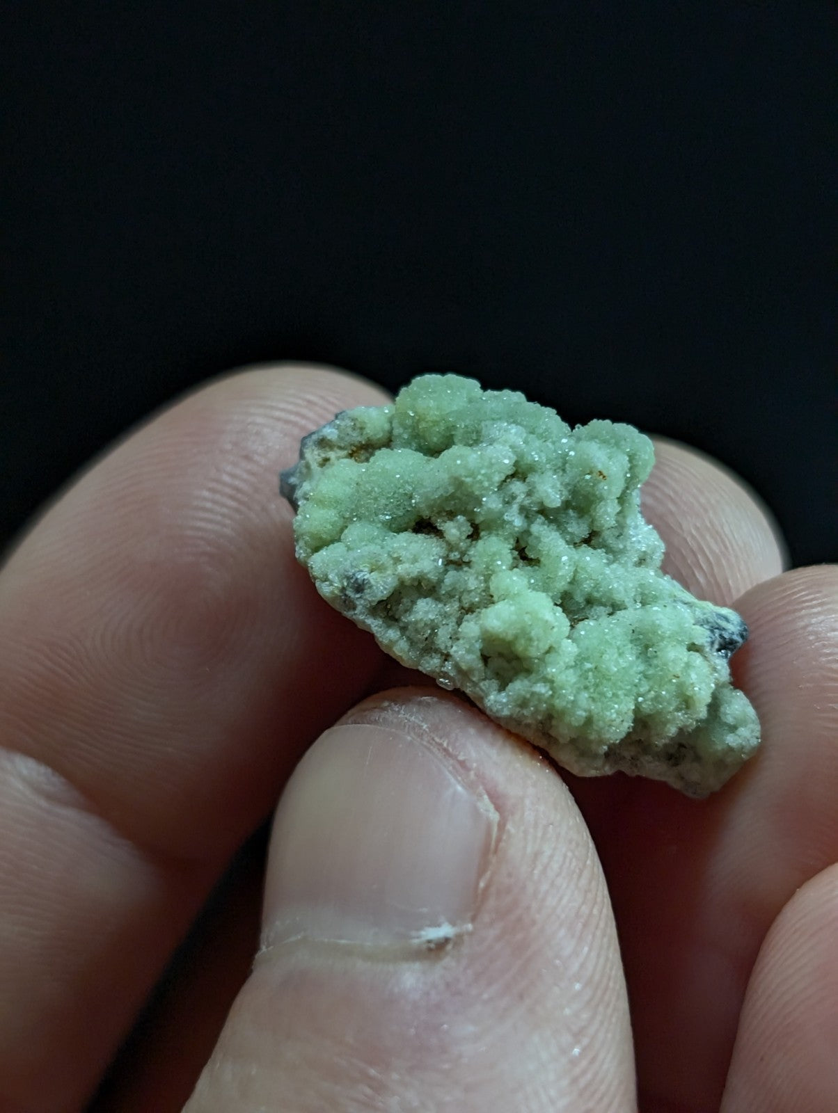 A textured, light green mineral specimen with a crystalline surface held between fingers.