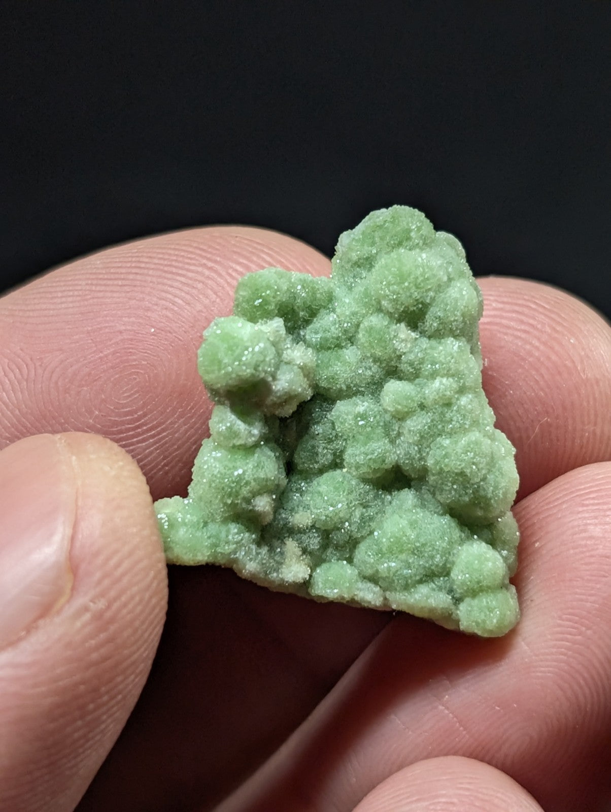 A small, light green mineral specimen with a rough, bubbly texture and clustered growths.