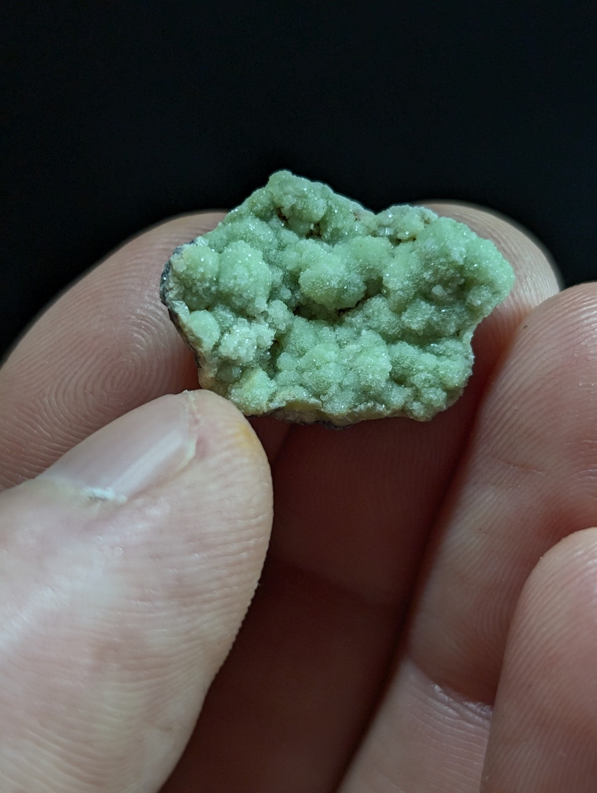 A pale green, textured mineral specimen with a rough, crystalline surface held between fingers.