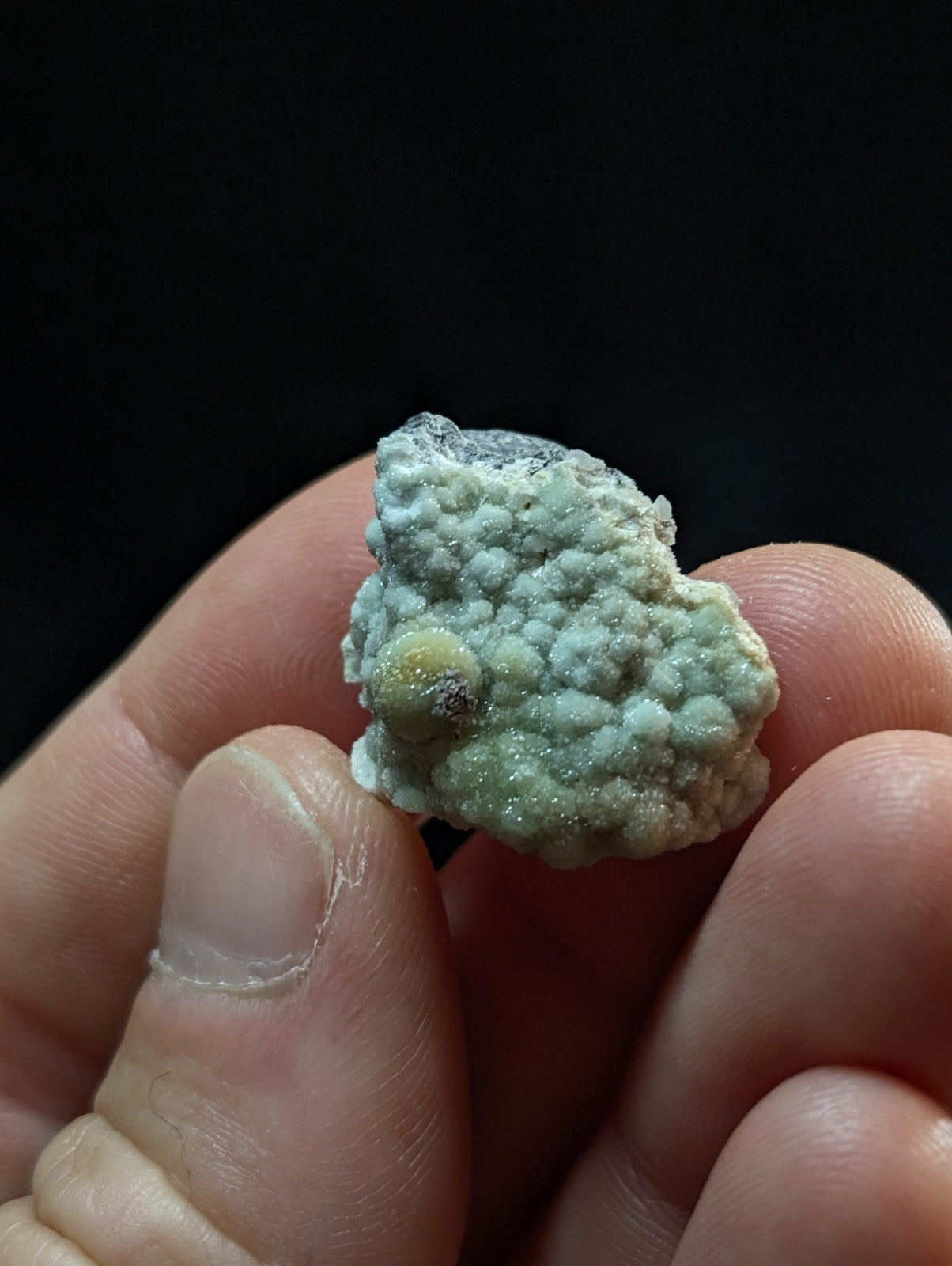 A textured, light green mineral specimen with a bumpy surface and small yellowish nodules.