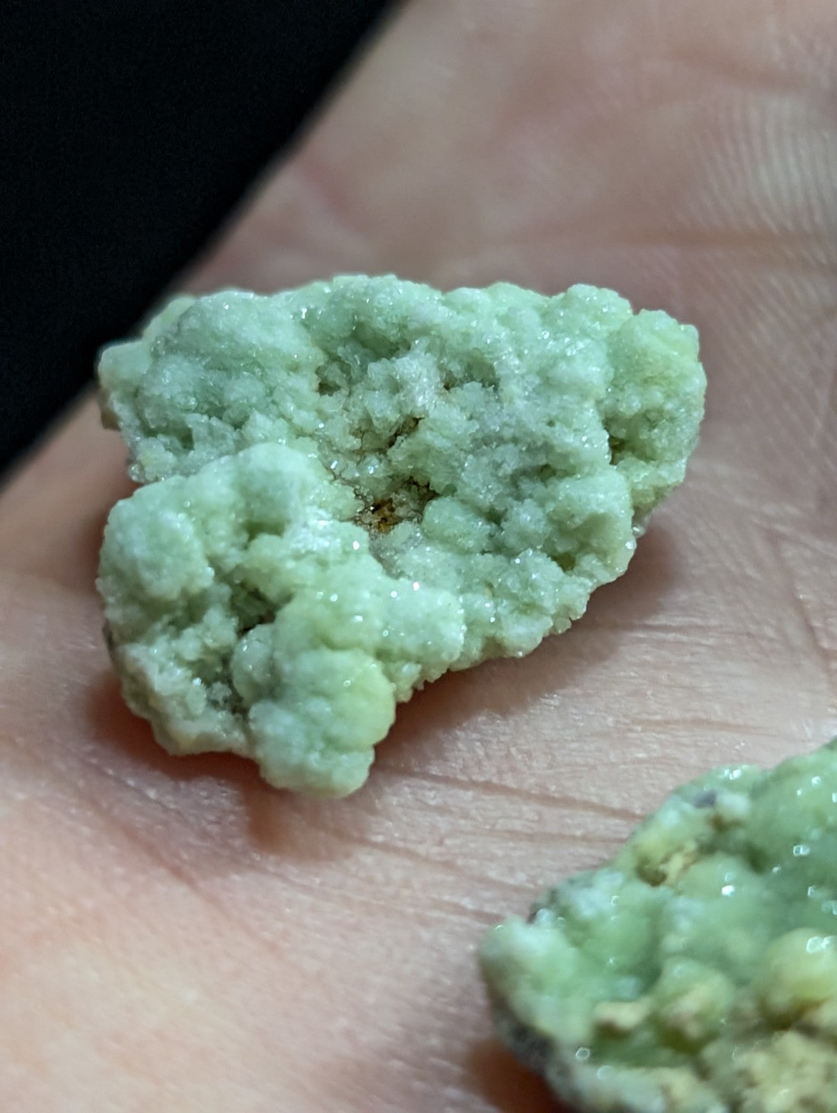 A pale green, crystalline mineral specimen with a rough, textured surface resting on skin.