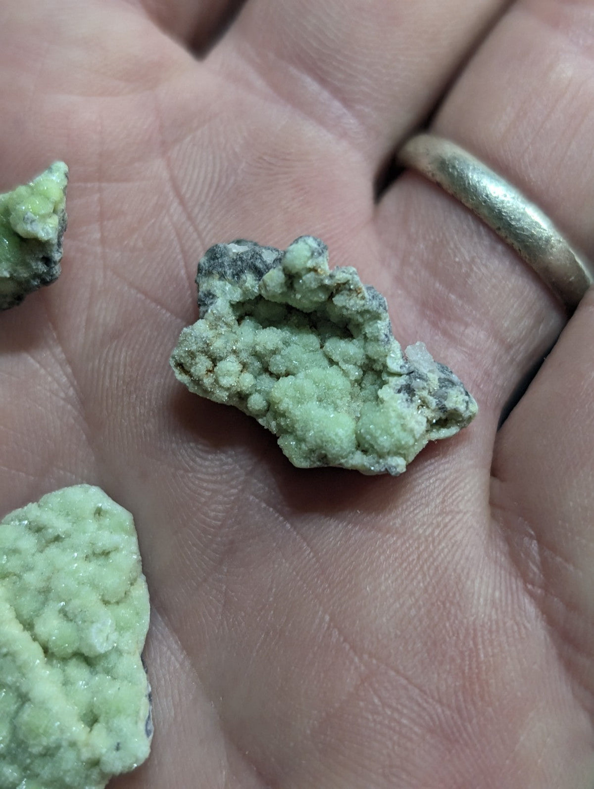 A hand holds several irregularly shaped, light green mineral specimens with a rough, crystalline texture and some darker grayish patches.