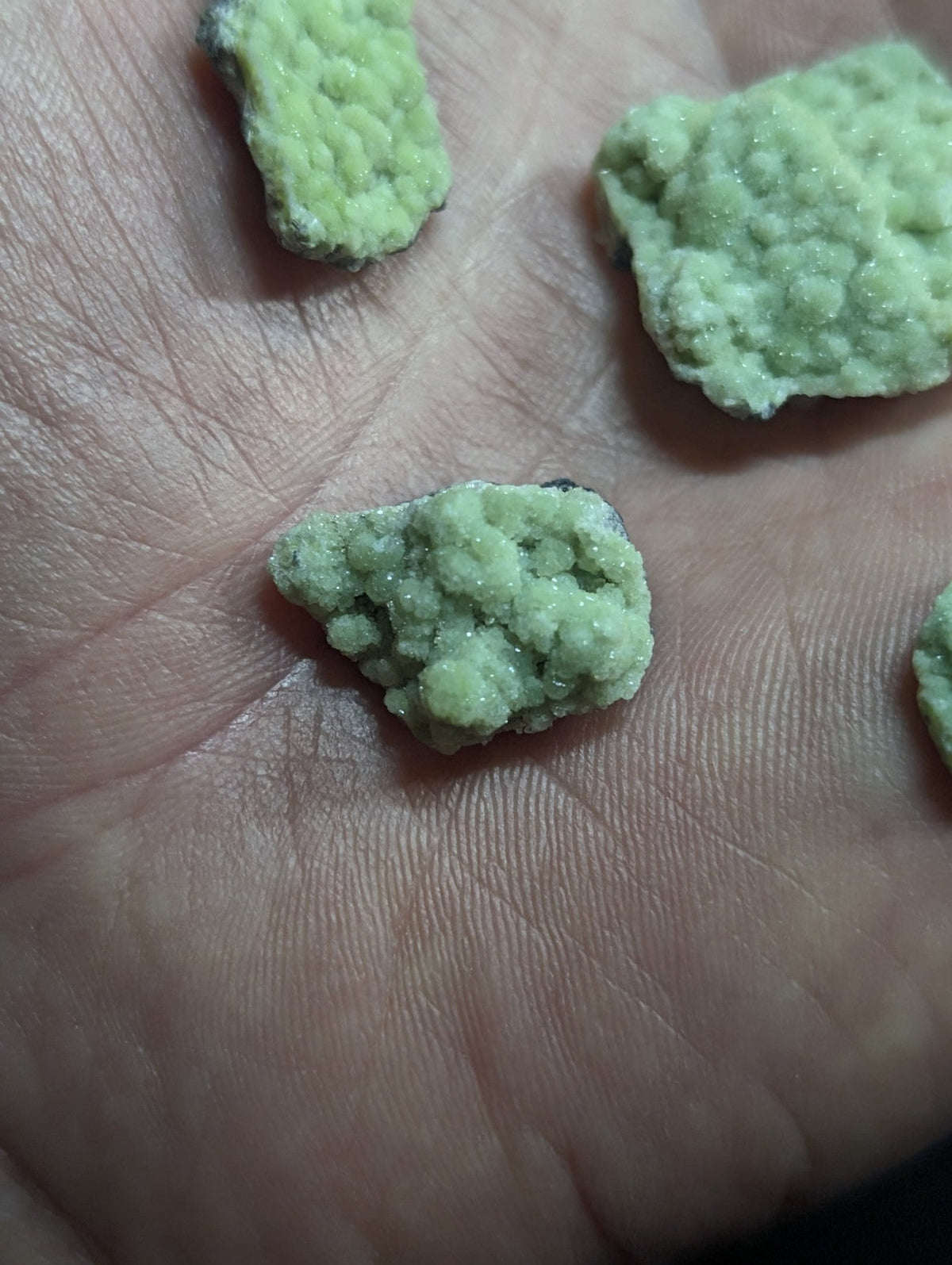 Light green, crystalline rock fragments resting in an open palm.