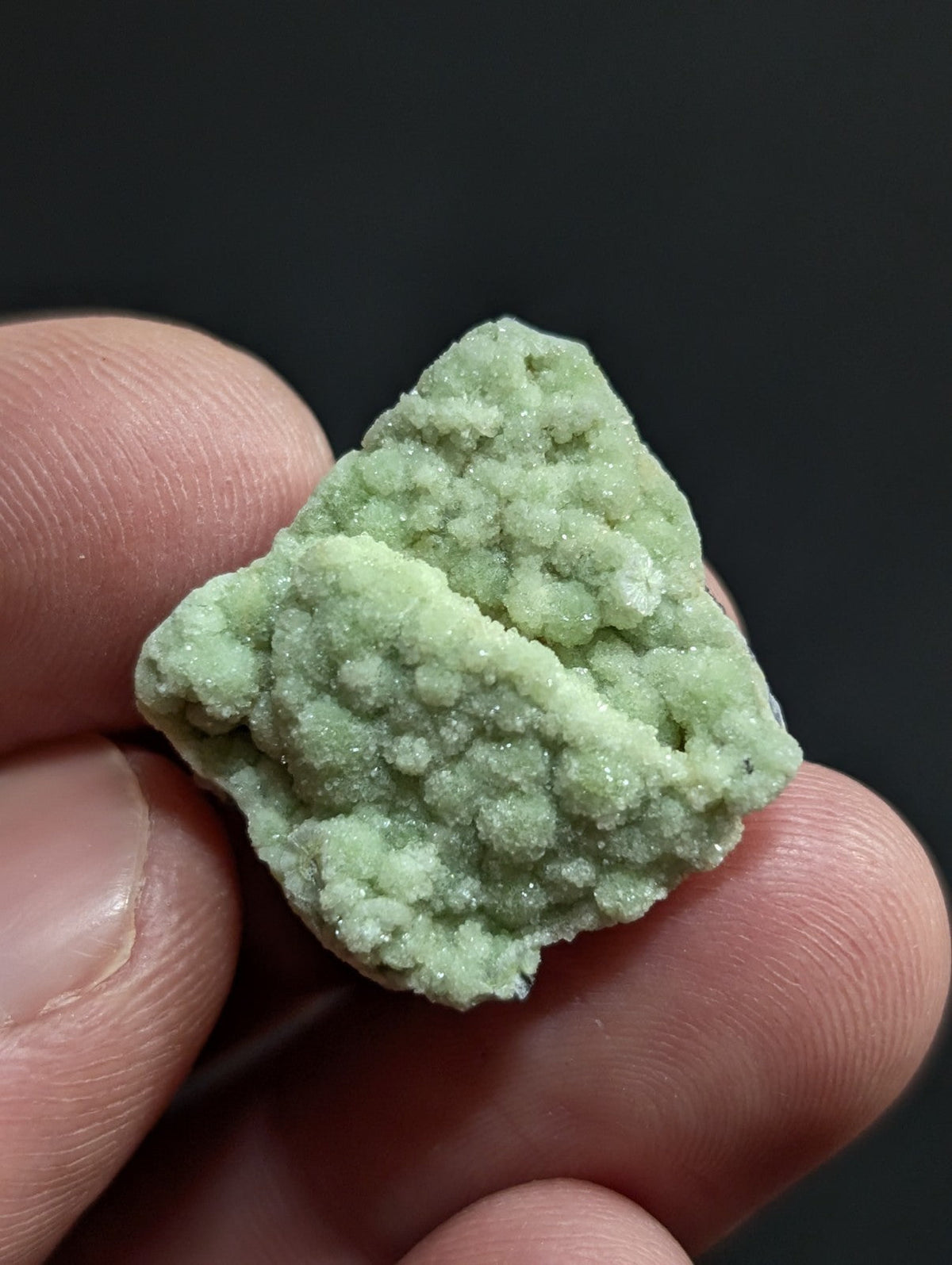 A pale green, crystalline mineral specimen with a rough, textured surface held between fingers.