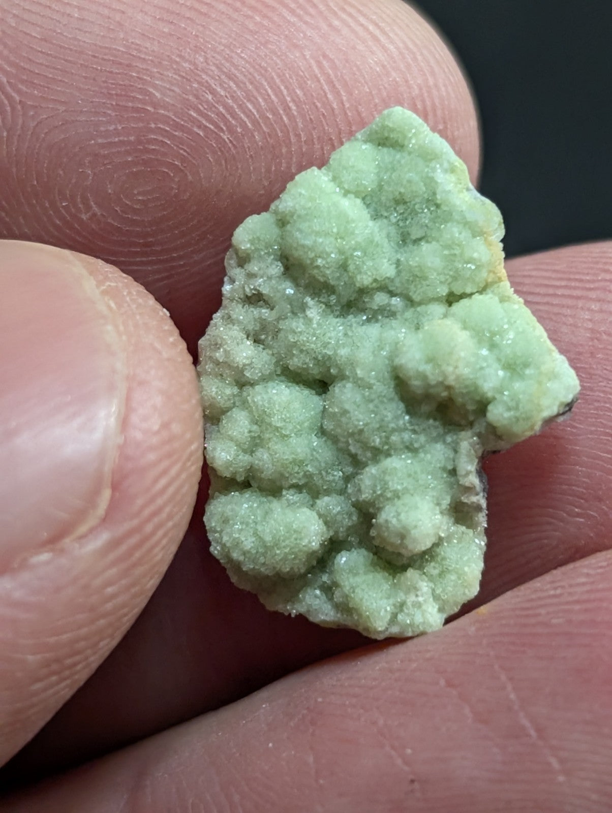 A pale green, textured mineral specimen with a crystalline, bumpy surface held between fingers.