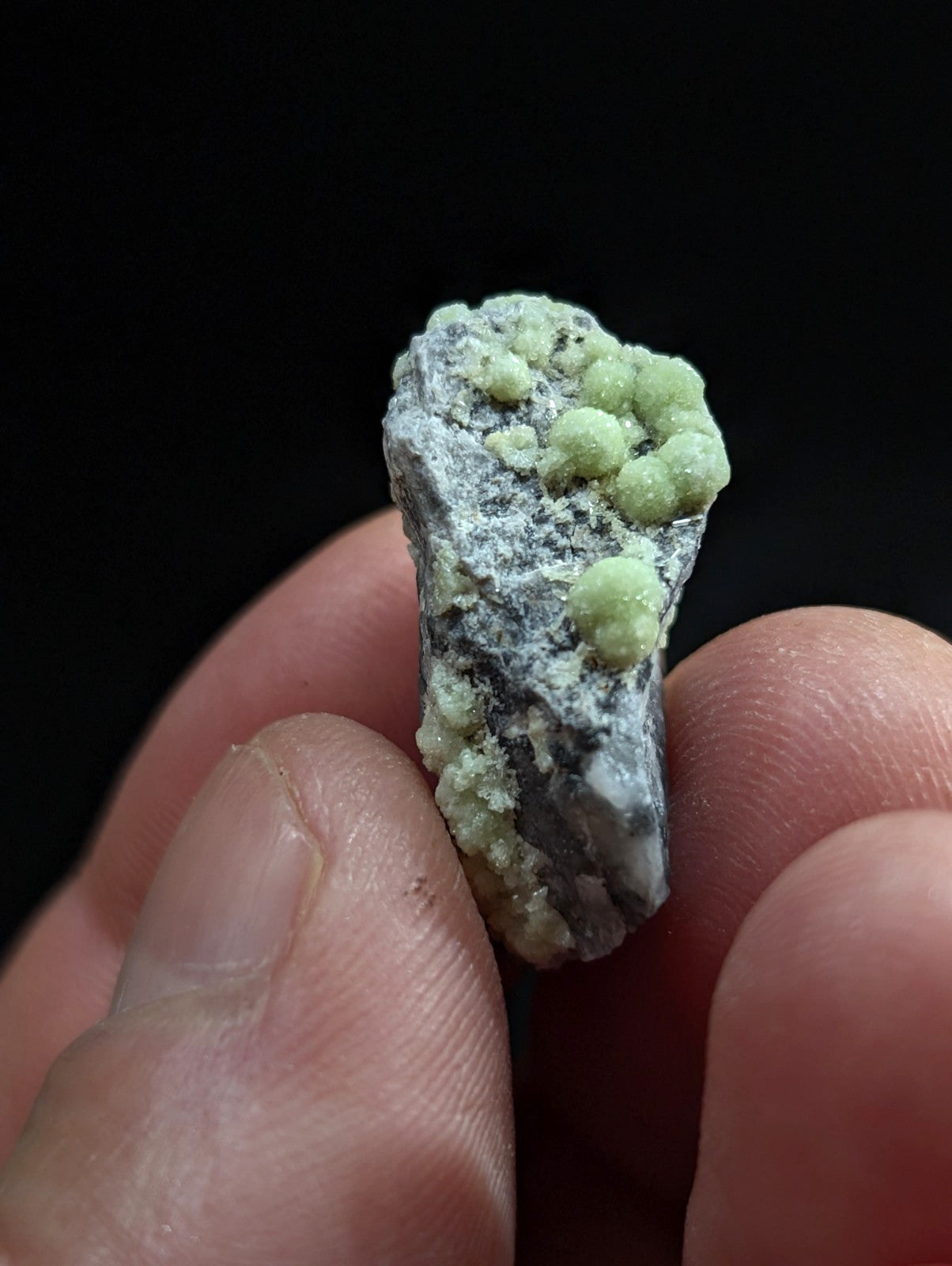 A small, irregularly shaped mineral specimen with a grayish base and clusters of light green crystalline growths.