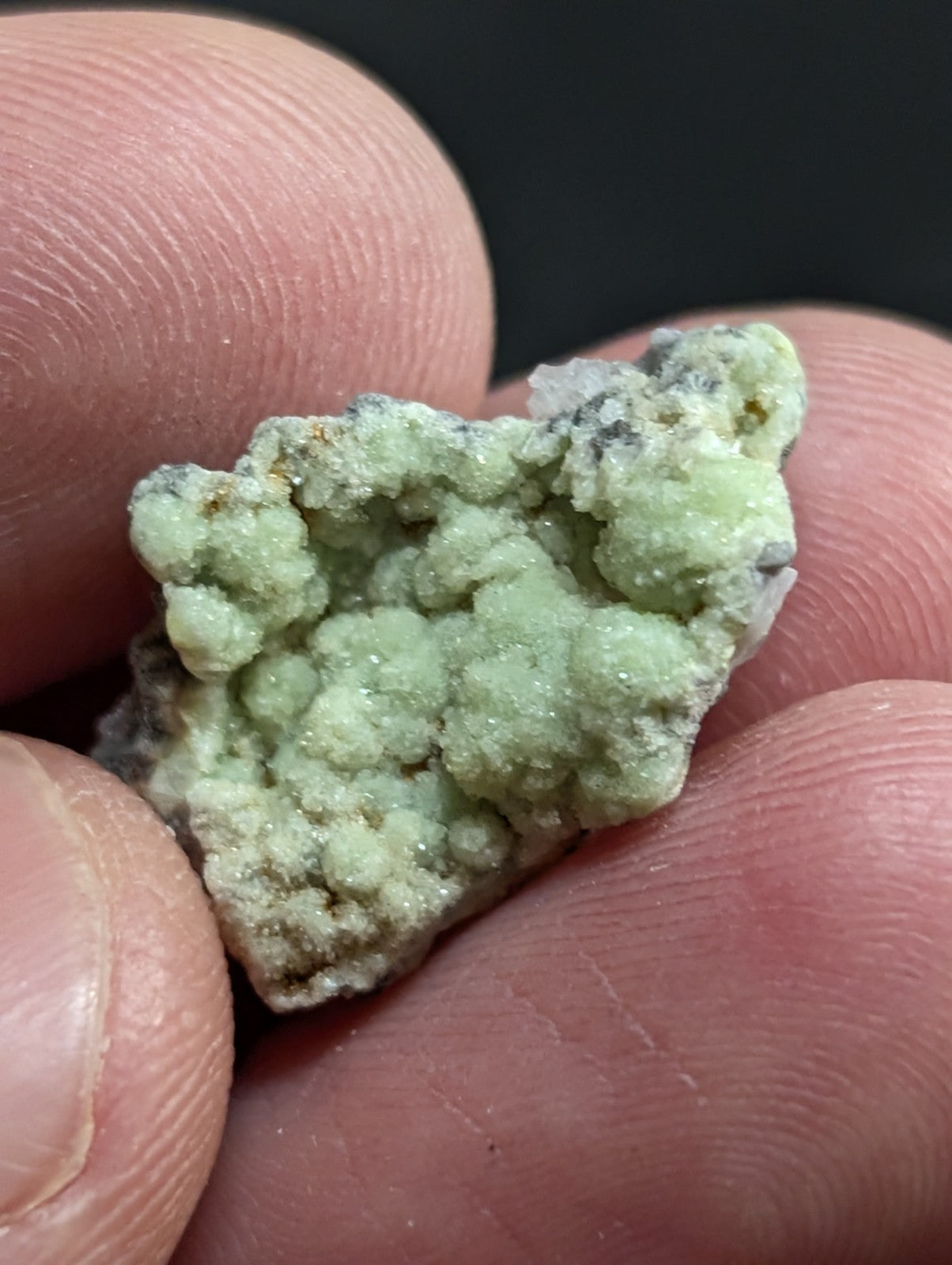 A pale green, textured mineral specimen with a crystalline surface held gently in fingers.