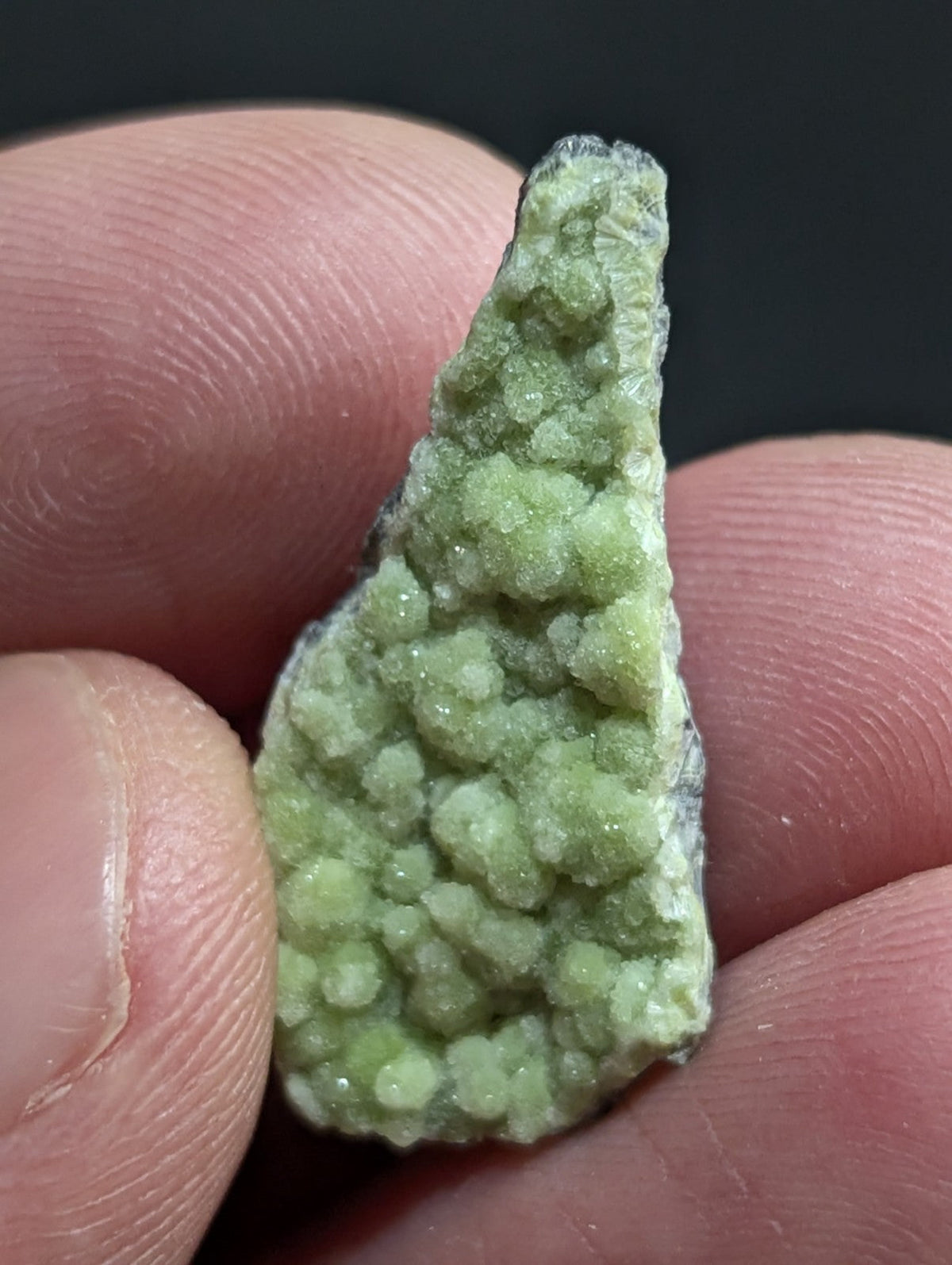 A pale green, textured mineral specimen with a crystalline surface held between fingers.