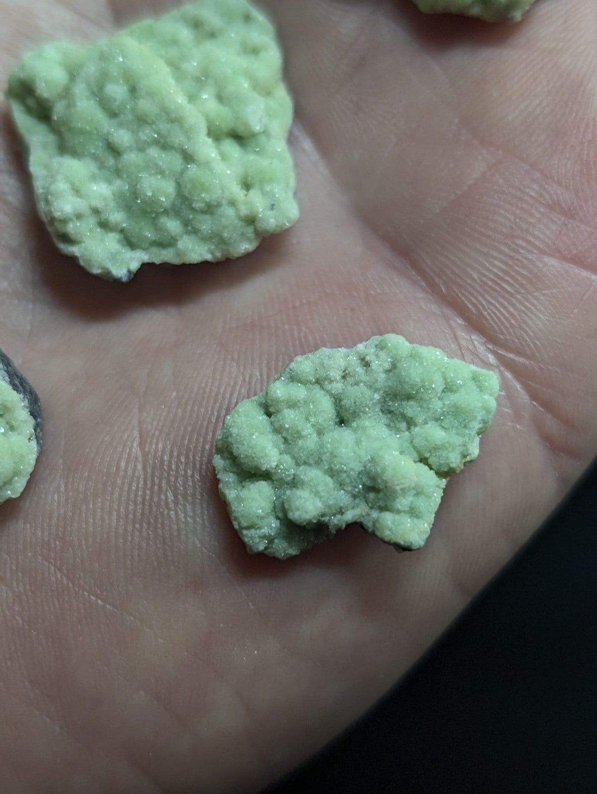 Light green, crystalline rock fragments resting on a palm.