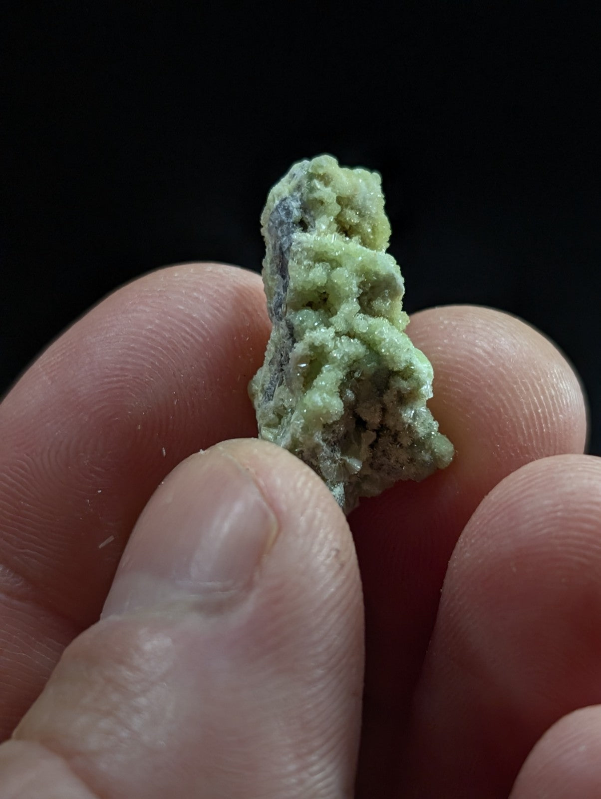 A textured, light green mineral specimen with a rough, crystalline surface held between fingers.