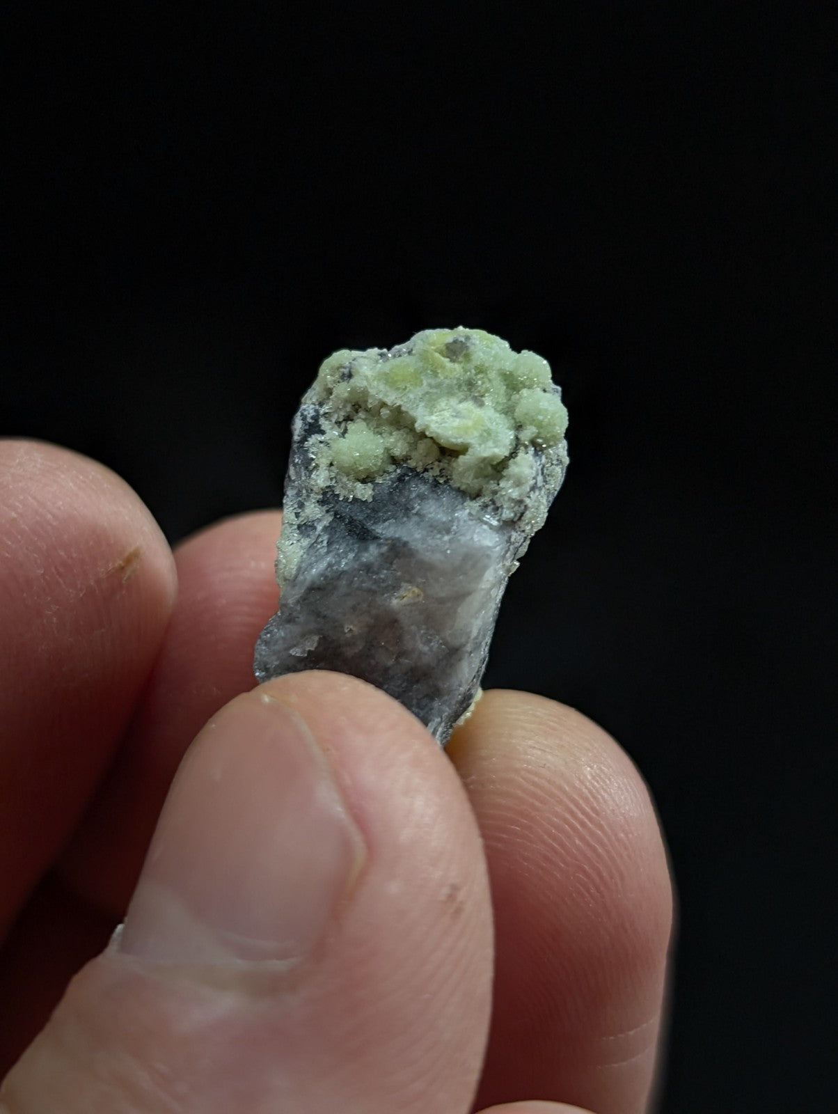 A rough, irregularly shaped mineral specimen with a dark gray base and patches of light green crystalline growths.