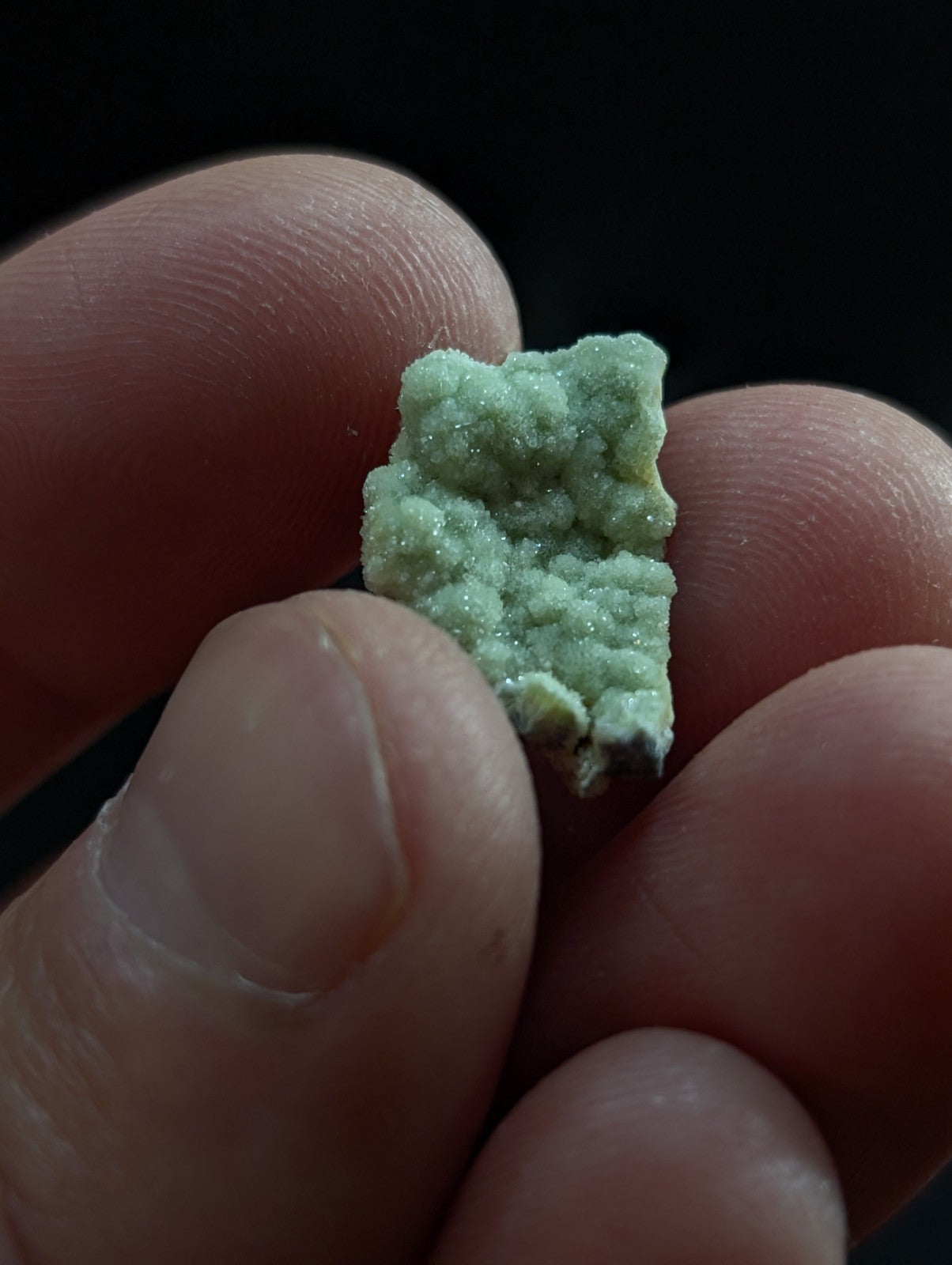A small, textured green mineral specimen with a crystalline surface.