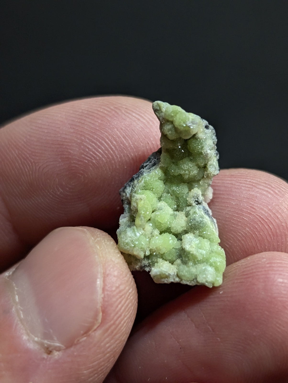 A small, light green mineral specimen with a textured, crystalline surface and darker grayish base.