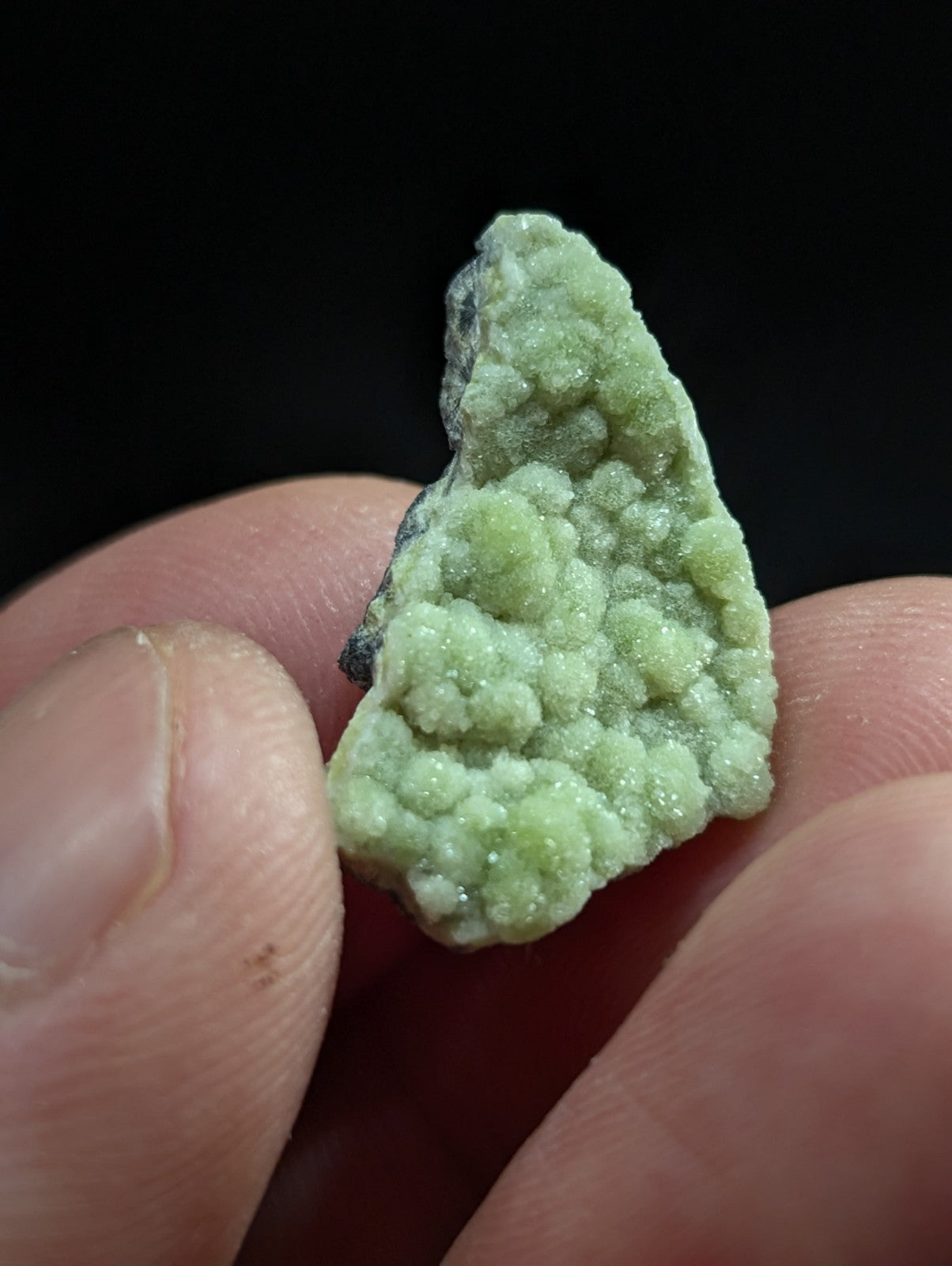 A pale green, textured mineral specimen with a crystalline surface held between fingers.