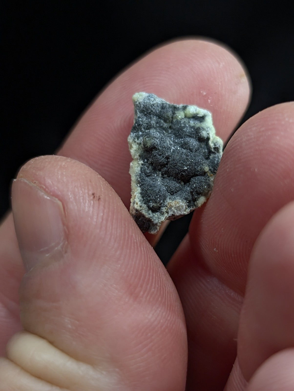 A small, irregularly shaped mineral specimen with a dark gray core and patches of greenish patina on its surface.
