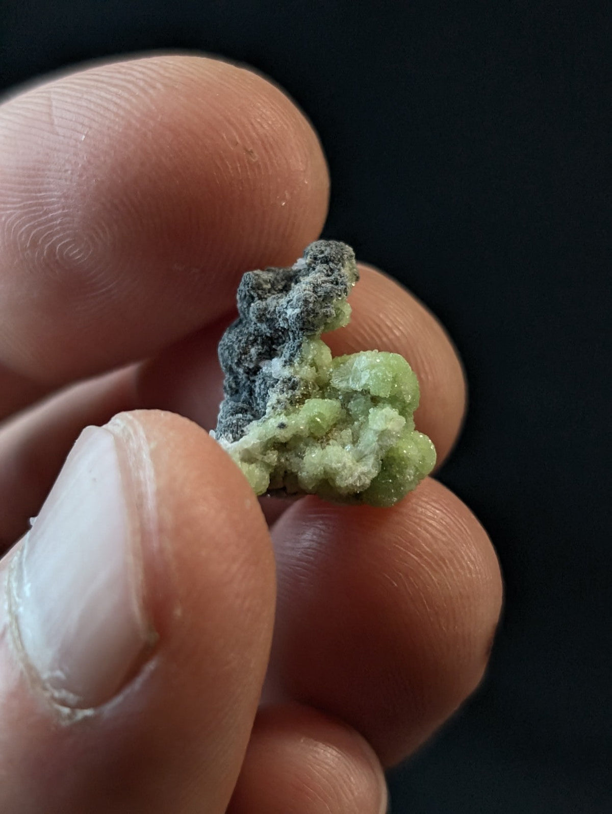 A small, irregularly shaped mineral specimen with a vibrant green crystalline structure and patches of dark grayish material.
