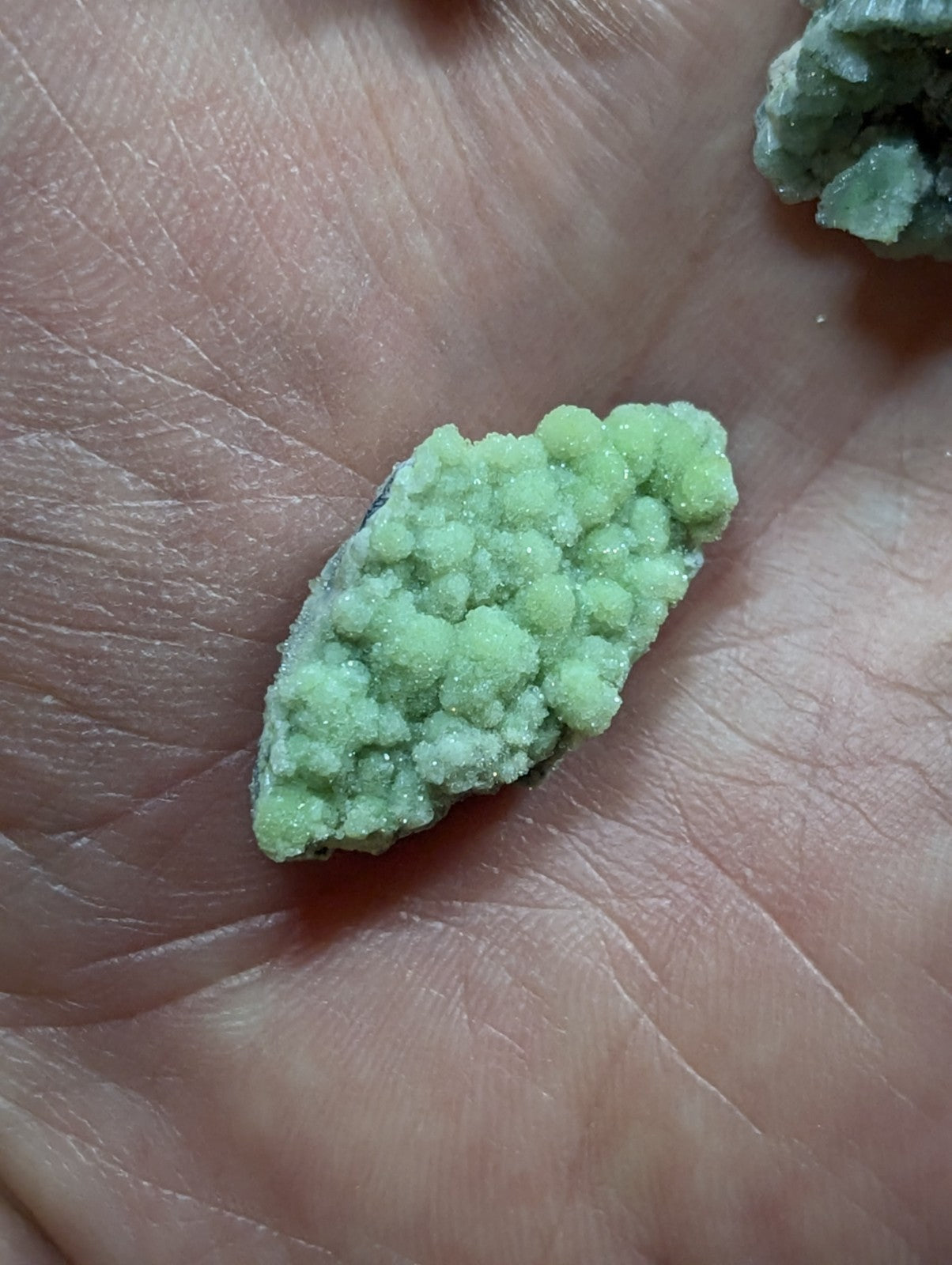 A pale green, crystalline mineral specimen with a rough, textured surface resting in the palm of a hand.