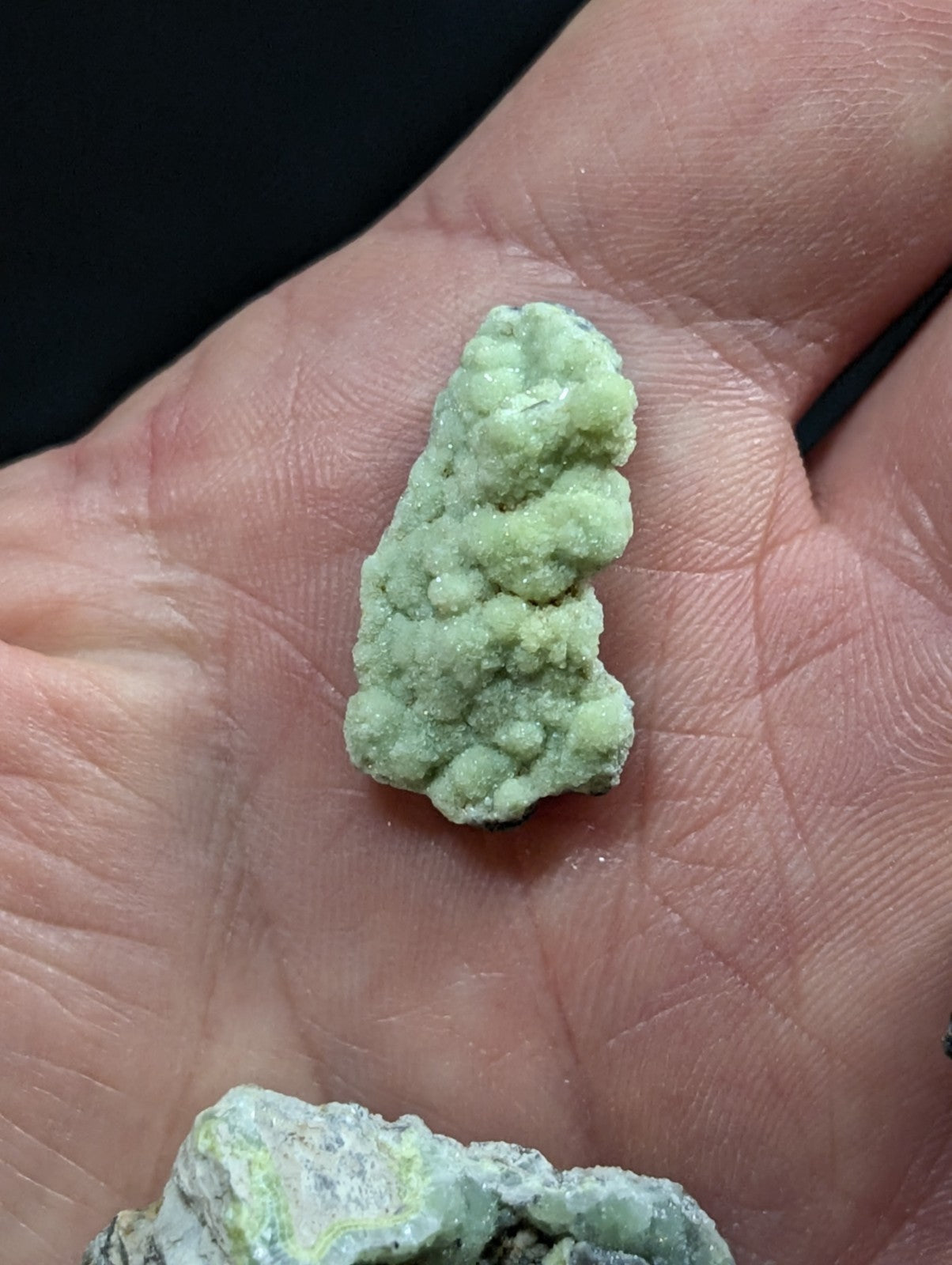 A pale green, textured mineral specimen with a bumpy, clustered surface resting in the palm of a hand.