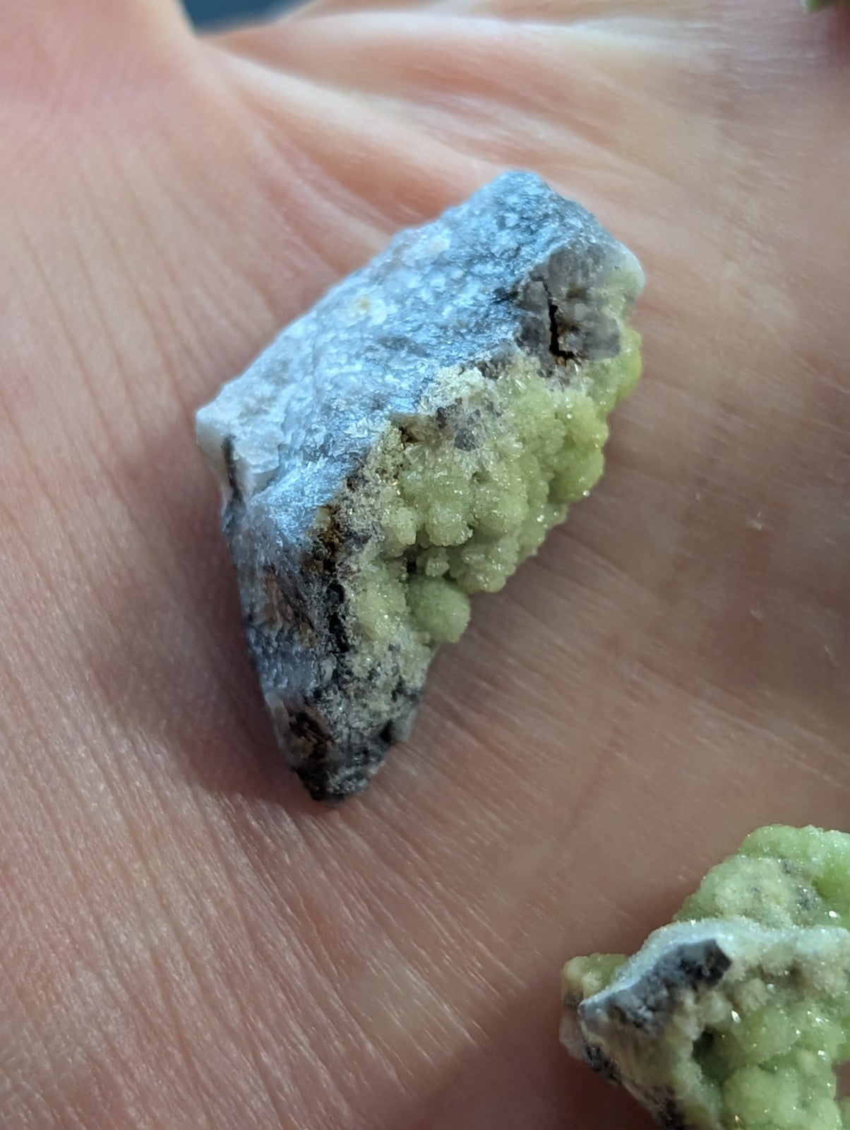 A rough, irregularly shaped mineral specimen with a grayish base and vibrant green crystalline growths.