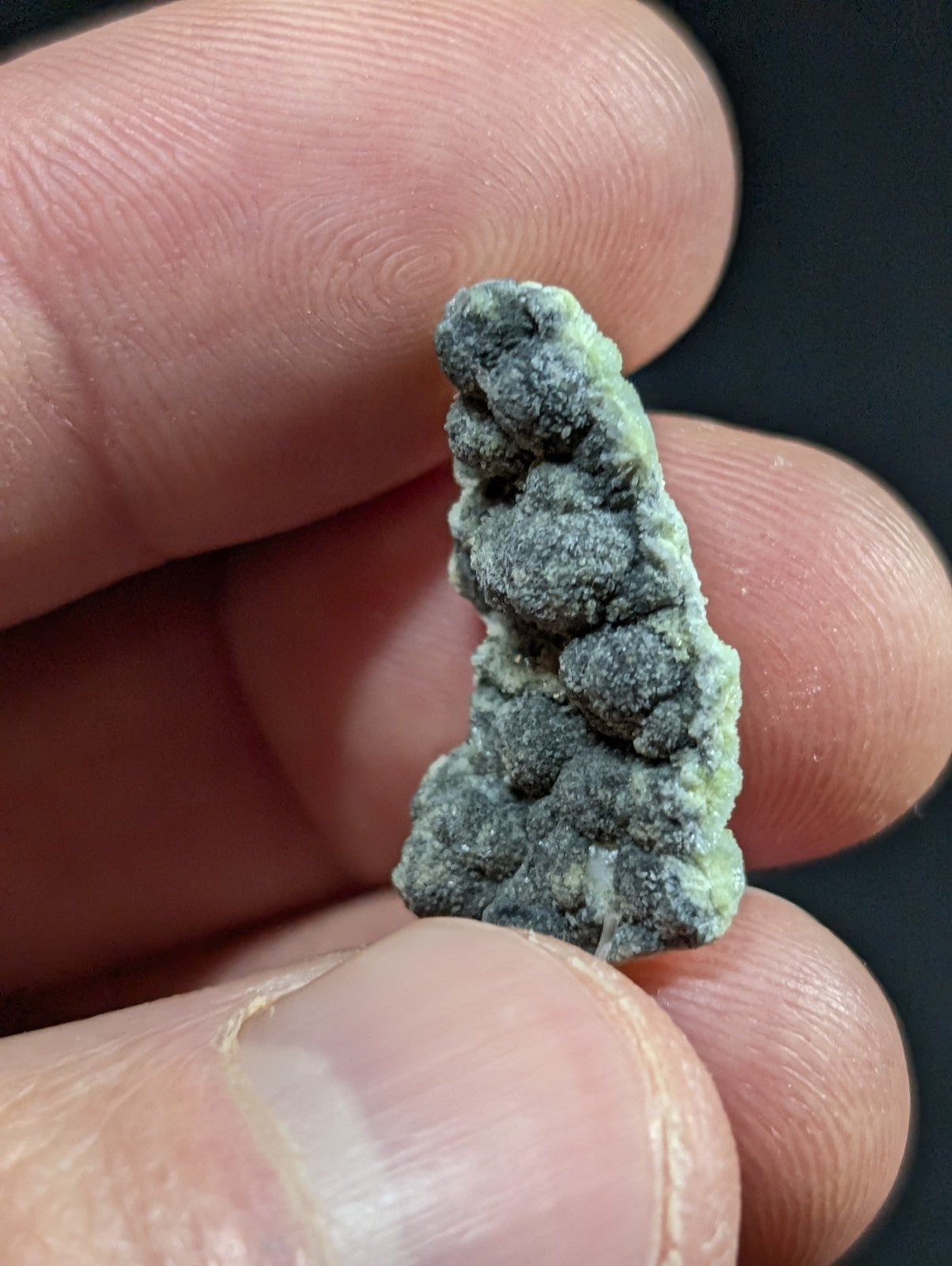 A textured, irregularly shaped mineral specimen with a mottled green and gray surface.
