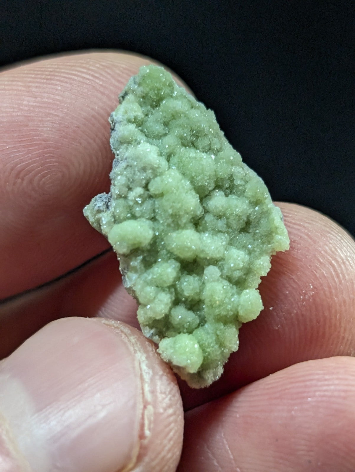 A pale green, crystalline mineral specimen with a rough, textured surface held between fingers.