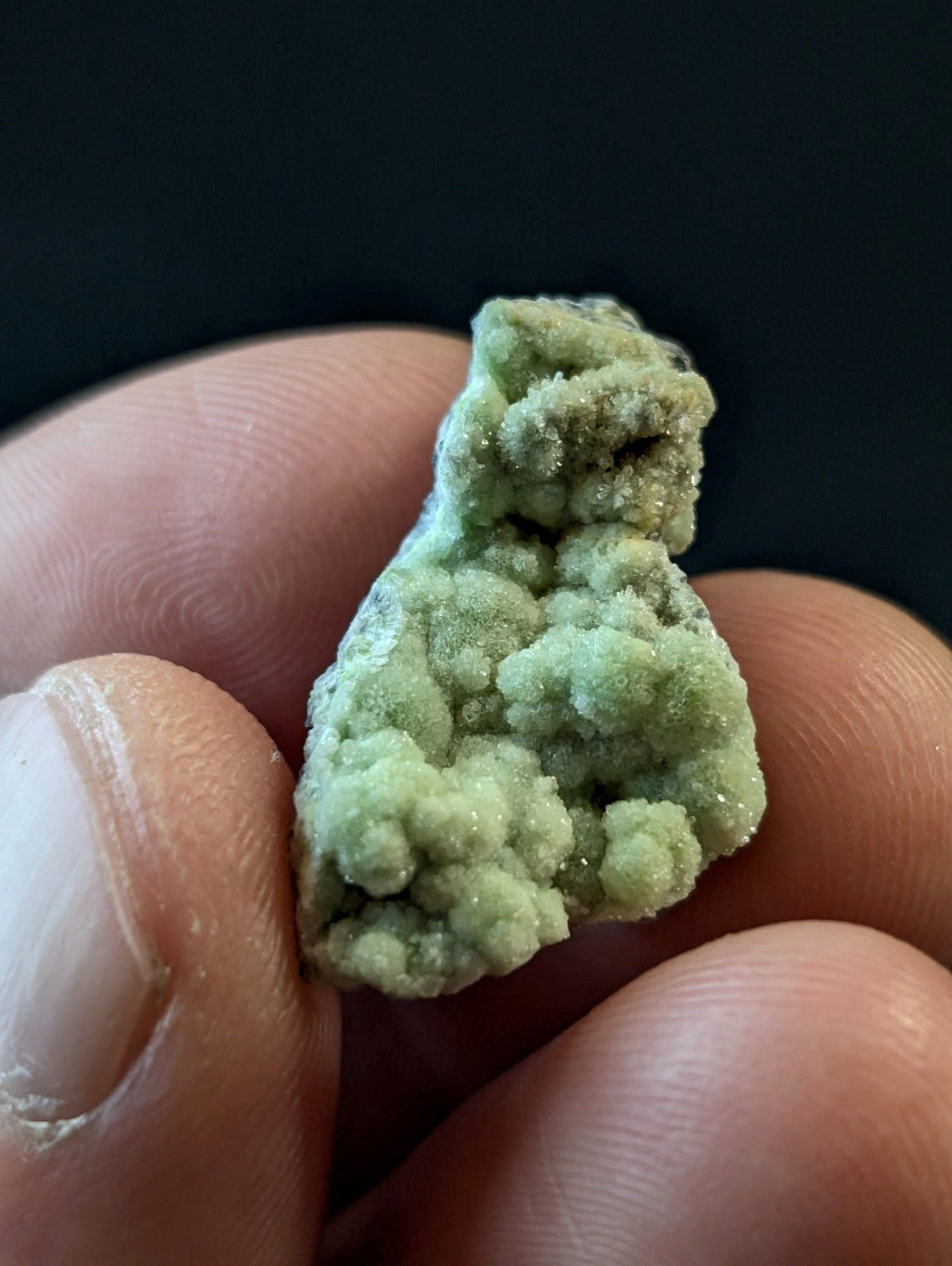 A textured, light green mineral specimen with a crystalline, bumpy surface held between fingers.
