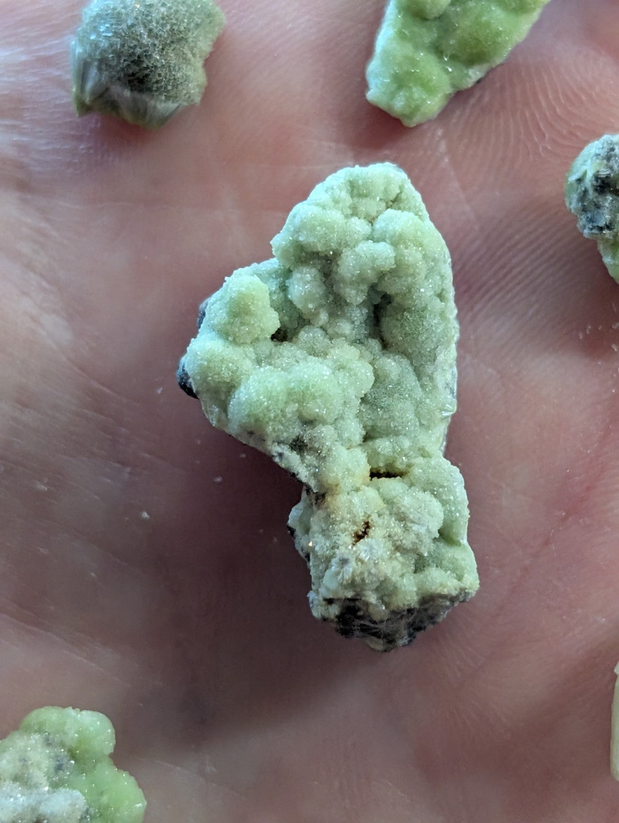 A pale green, crystalline mineral specimen with a rough, textured surface and dark inclusions.