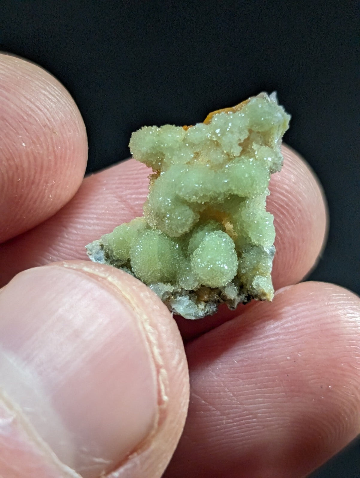 A delicate, light green mineral specimen with a crystalline texture and subtle orange undertones.