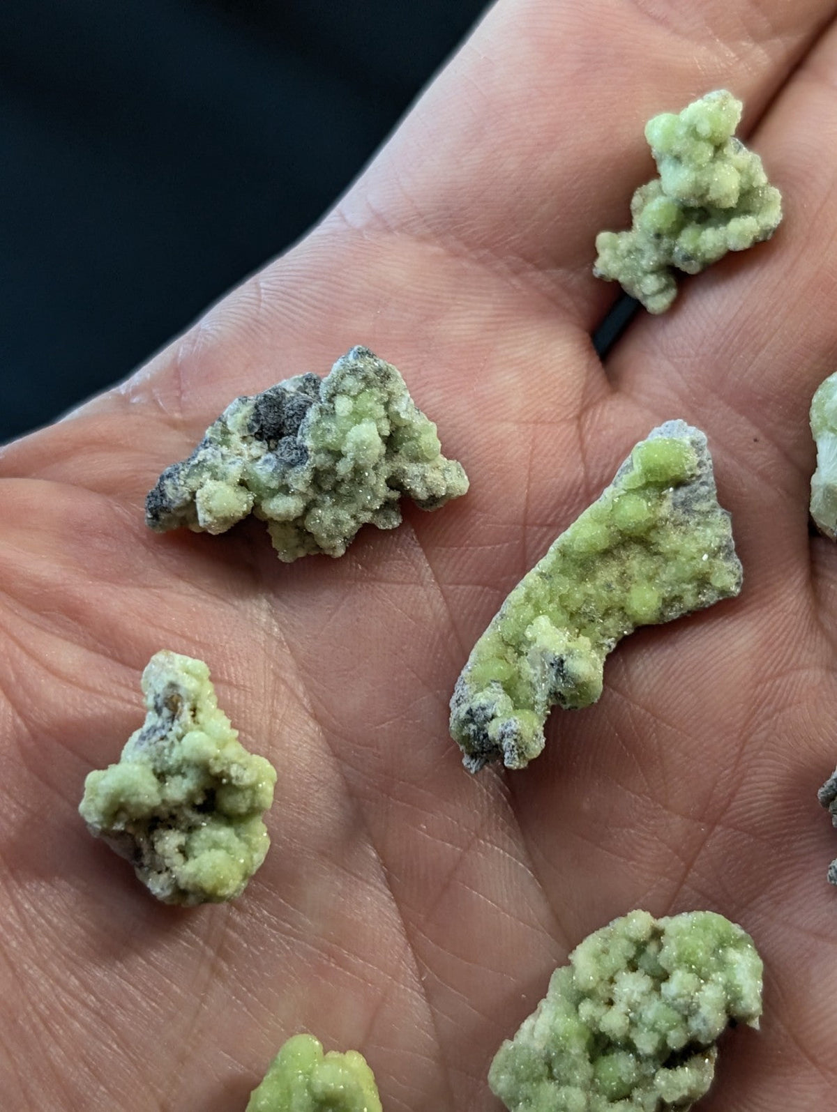 Light green, crystalline mineral specimens with speckles of dark gray resting in an open palm.