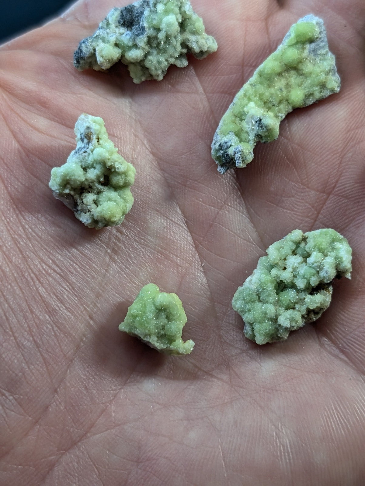 Light green, crystalline mineral specimens with a rough, textured surface and some darker speckles.