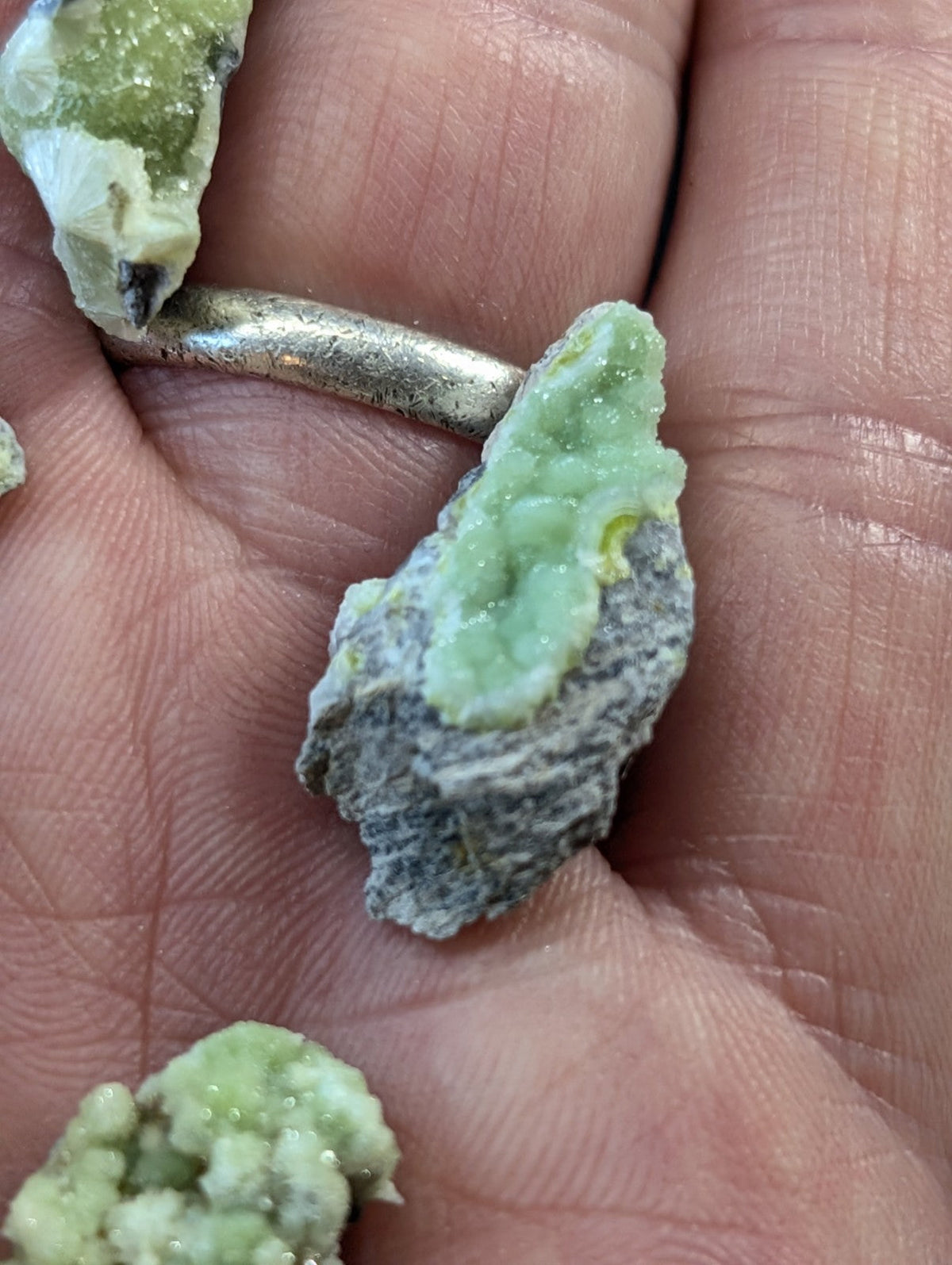 A hand holds a silver ring with a rough, green mineral specimen nestled in its band.