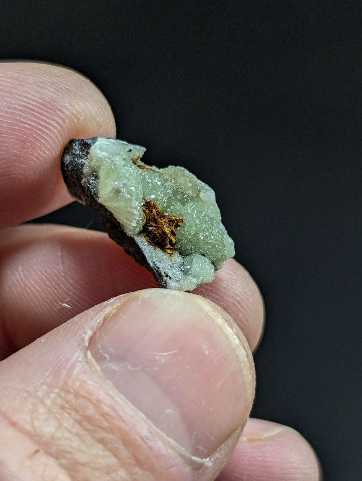 A rough, pale green mineral specimen with a crystalline texture and dark matrix.