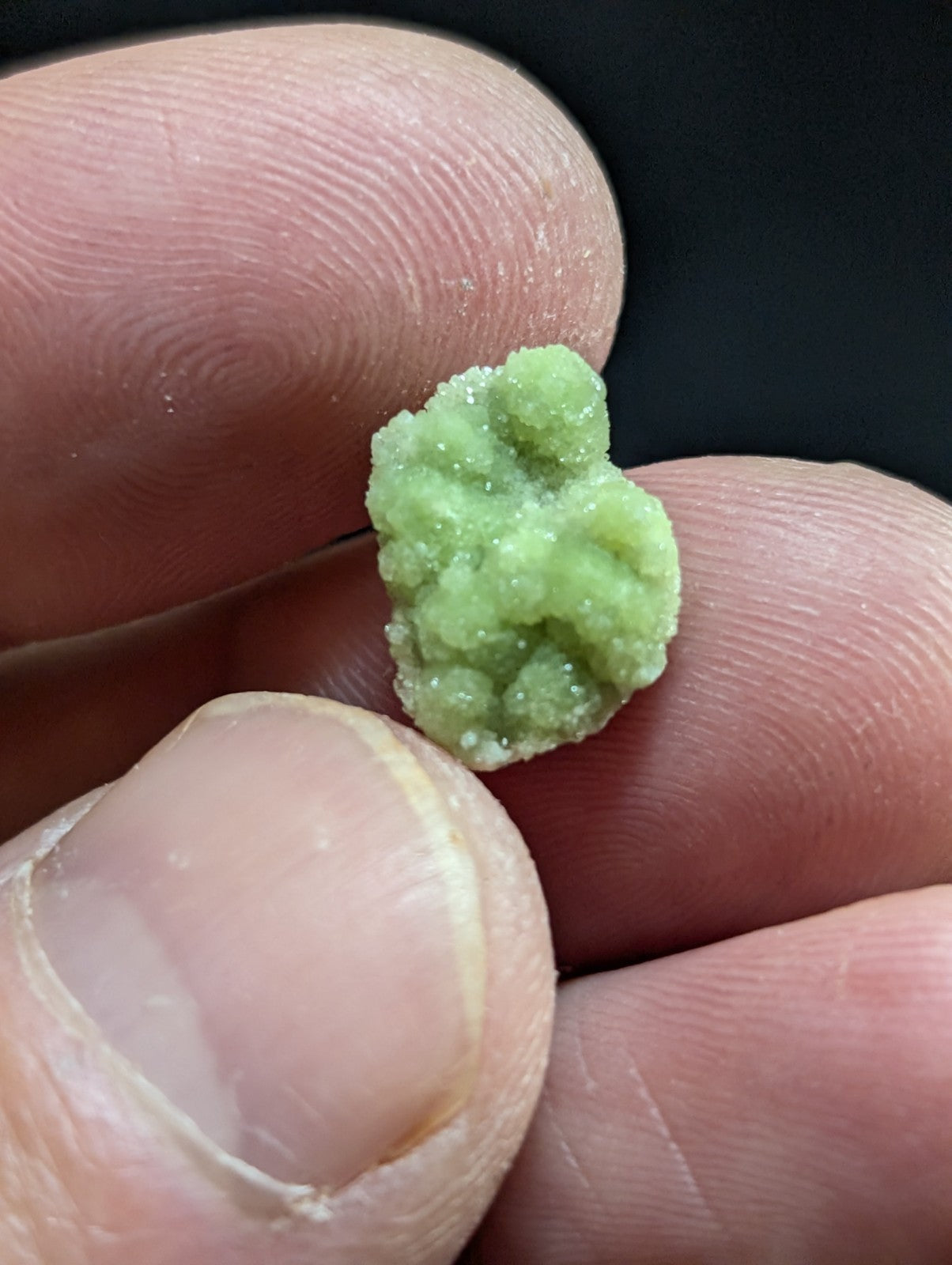 A small, light green crystalline candy with a textured, sugary surface.