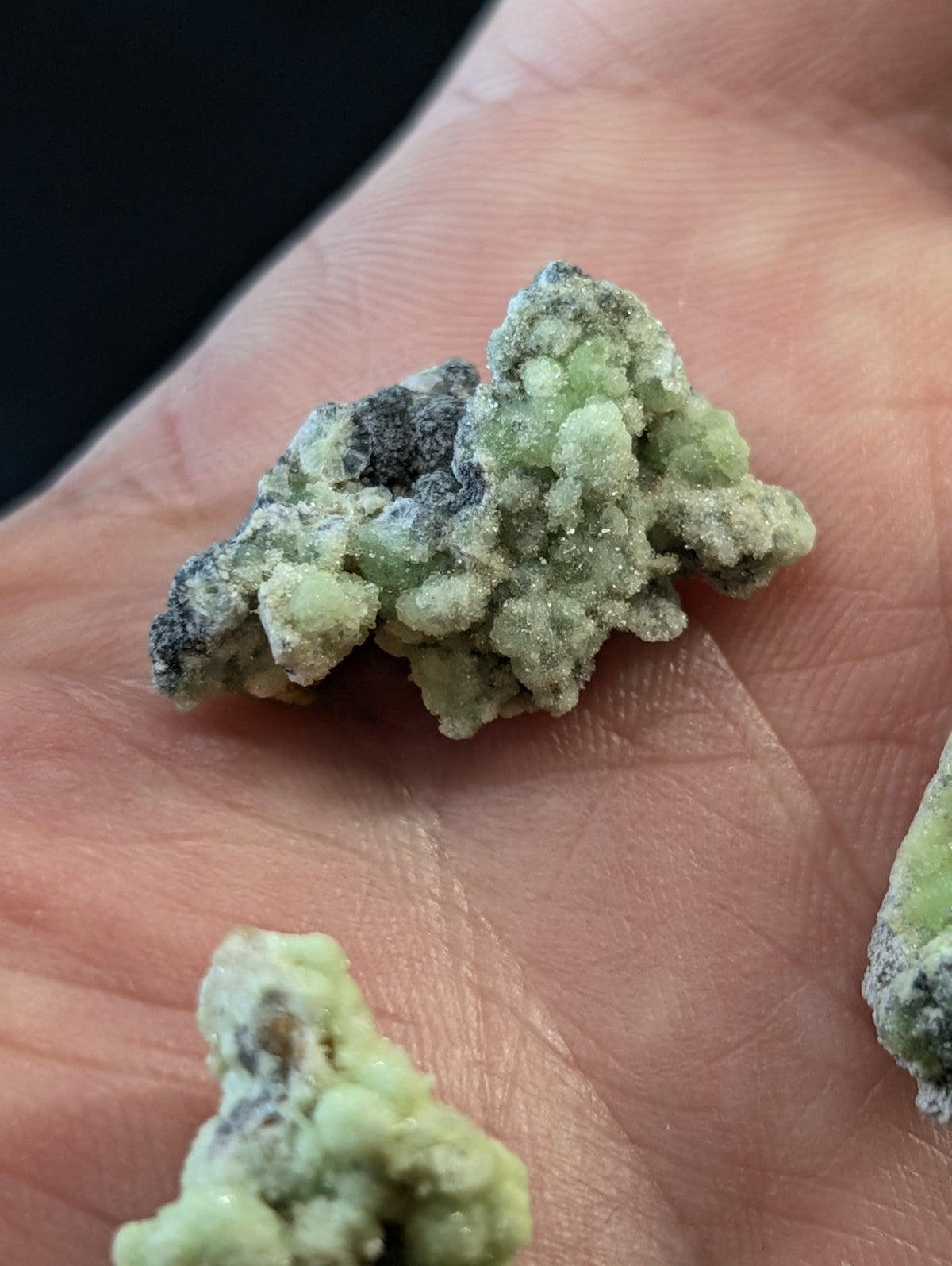 A cluster of pale green, crystalline mineral formations with dark gray patches resting in the palm.