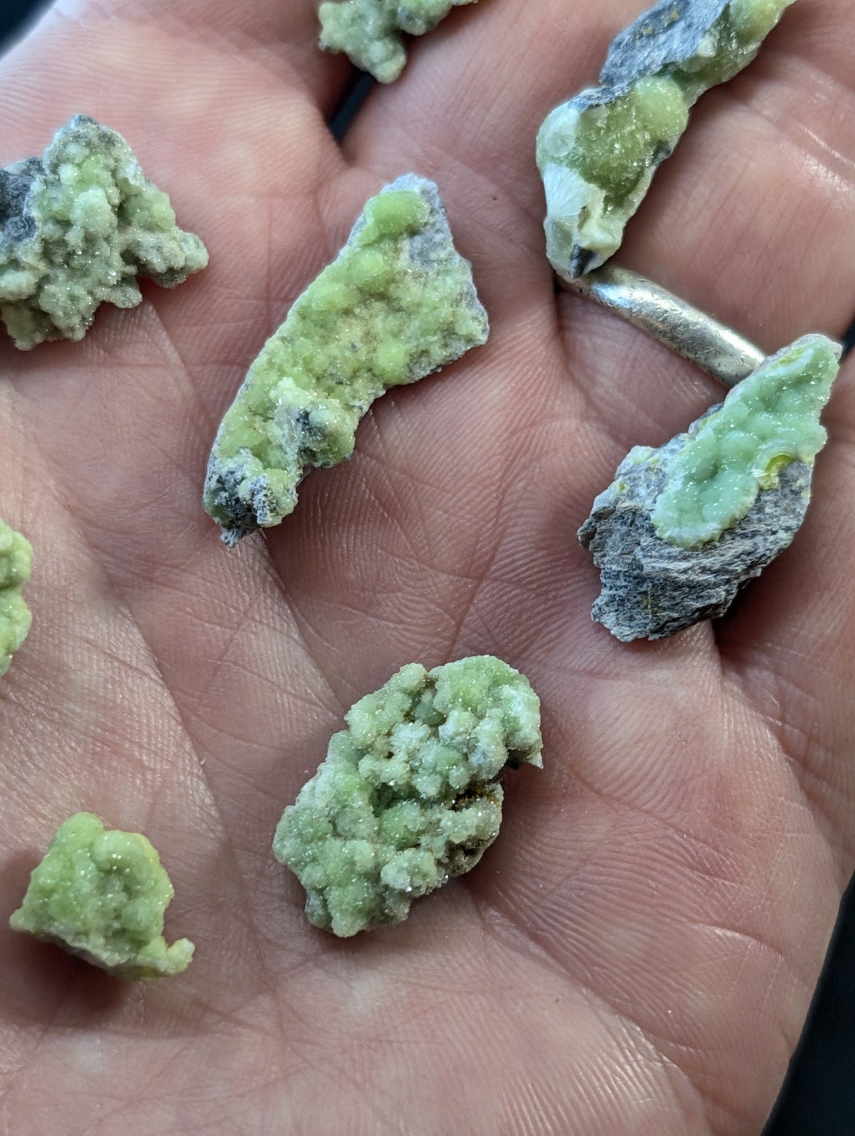 Green, crystalline mineral specimens with a rough, textured surface and some grayish patches.