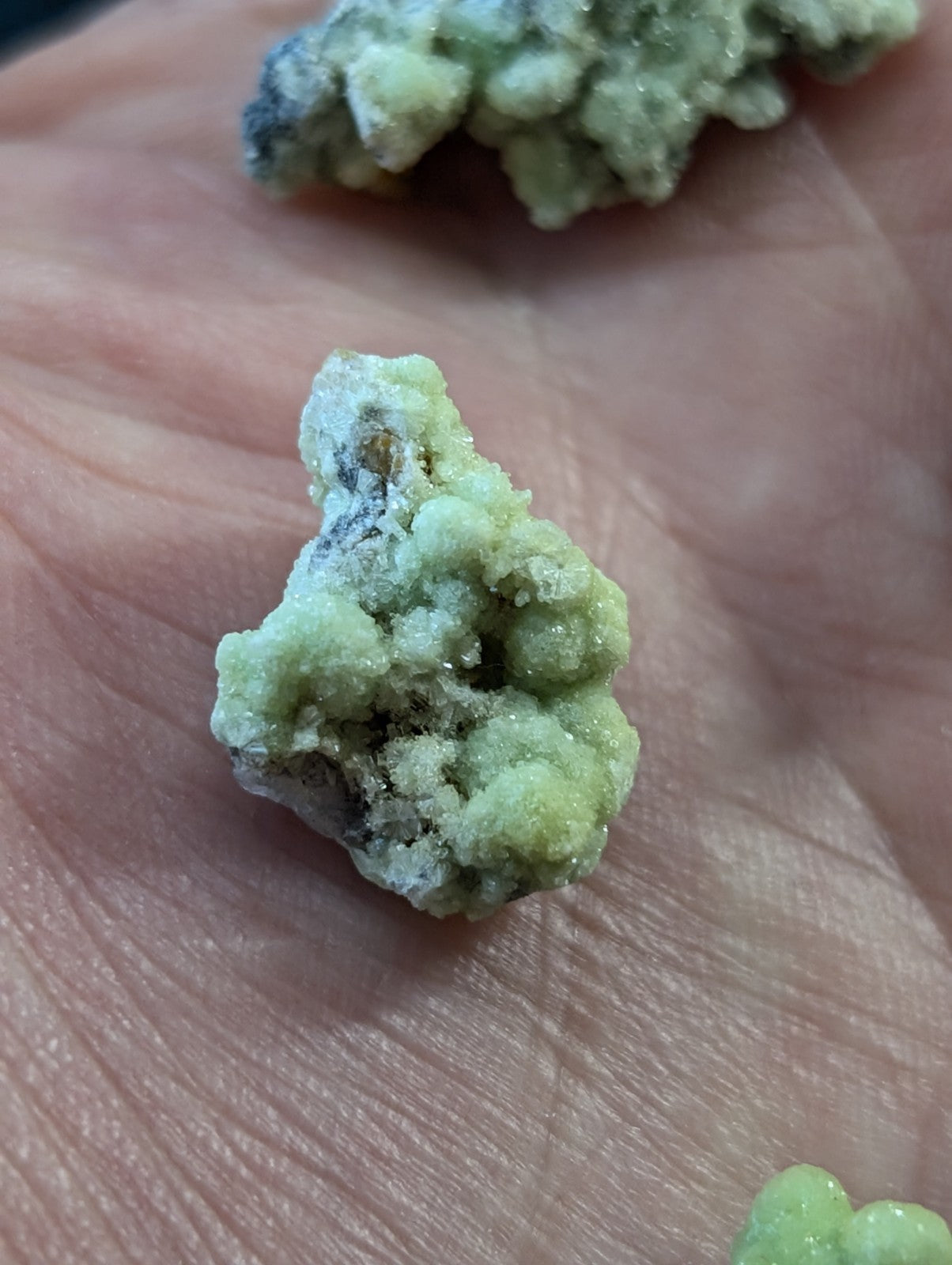 A pale green, crystalline mineral specimen with a rough, textured surface and subtle darker patches.