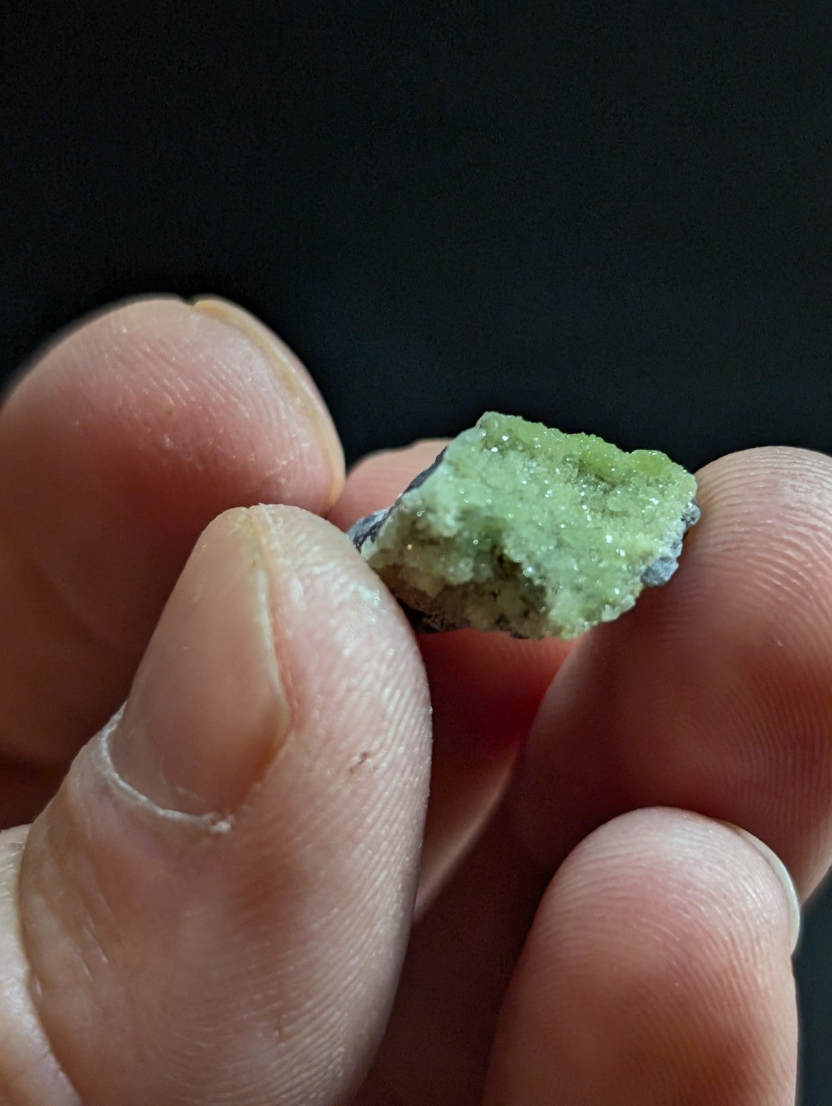 A small, rough-hewn green mineral specimen with a crystalline texture and hints of grayish matrix.