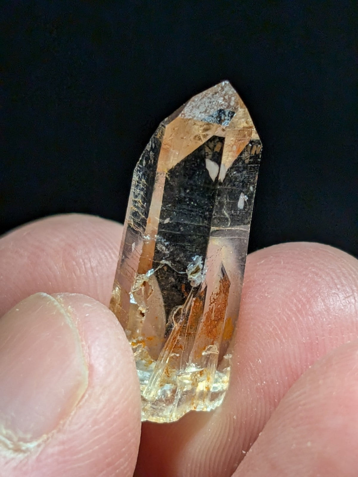 A translucent golden-orange quartz crystal with natural inclusions and a pointed, faceted tip.