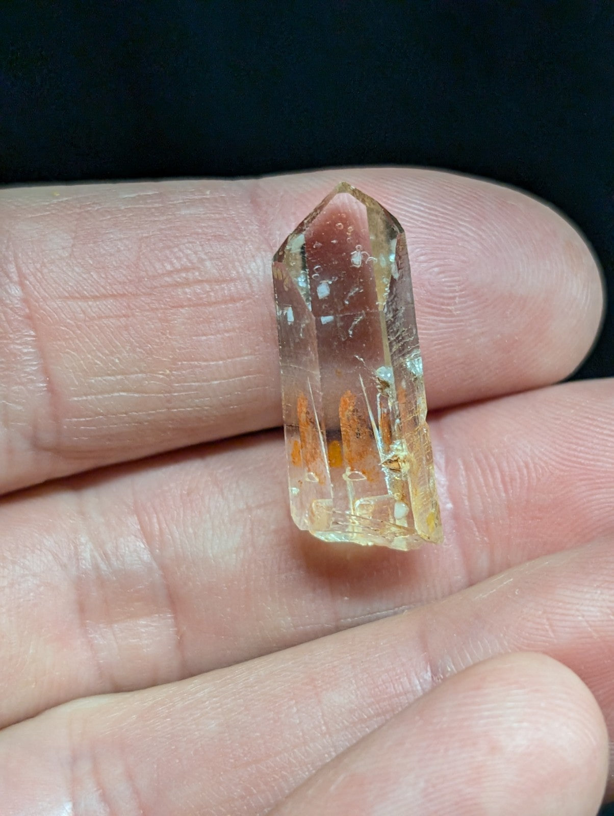 A translucent golden-yellow crystal with a pointed top and visible internal inclusions, held gently between fingers.