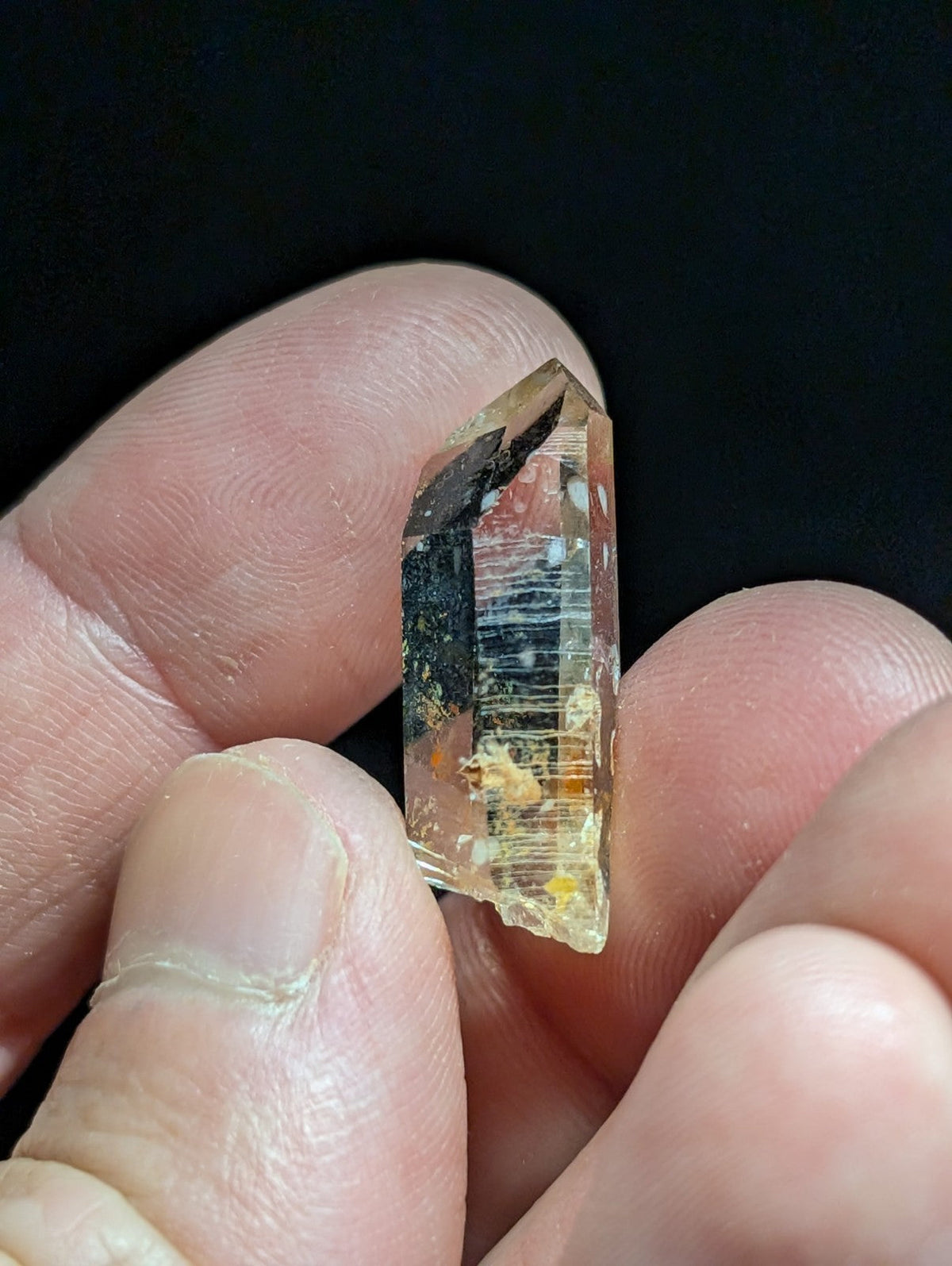 A translucent amber quartz crystal with dark inclusions and subtle internal striations, held delicately between fingers.