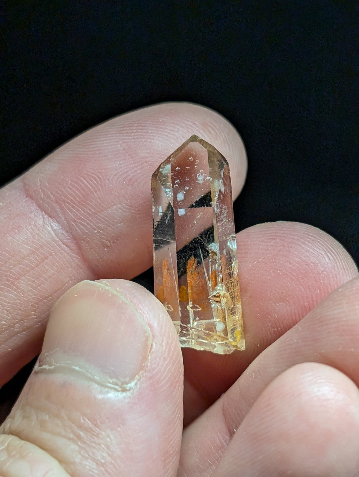 A translucent golden-yellow citrine crystal with a pointed top and natural inclusions, held delicately between fingers.