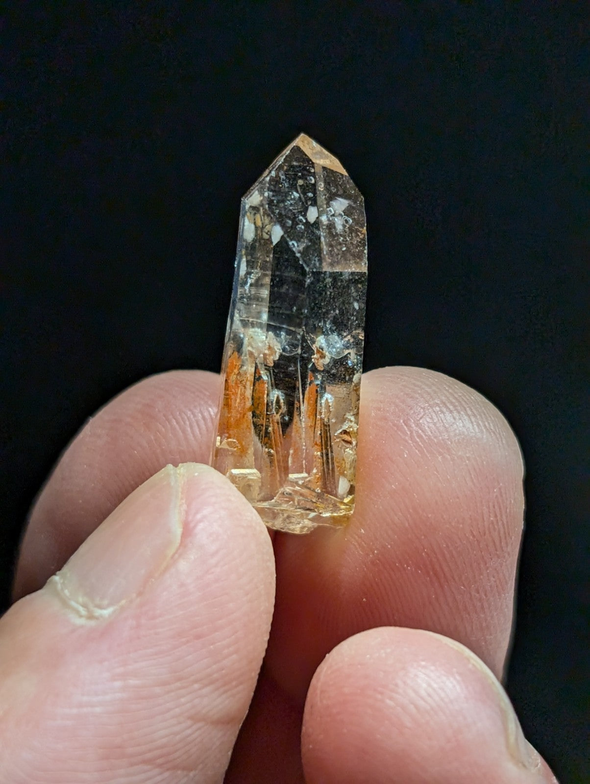 A translucent golden-yellow crystal with a pointed top and visible internal inclusions, held delicately between fingers.