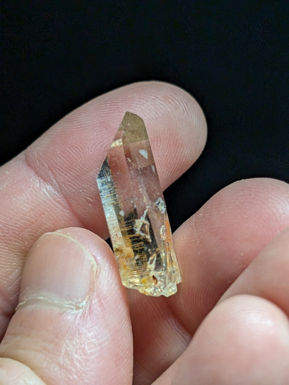 A translucent yellowish crystal with a pointed tip and visible internal inclusions, held gently between fingers.