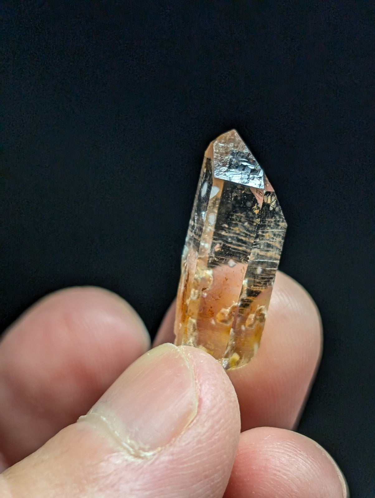A translucent orange crystal with natural inclusions and a pointed, faceted tip.