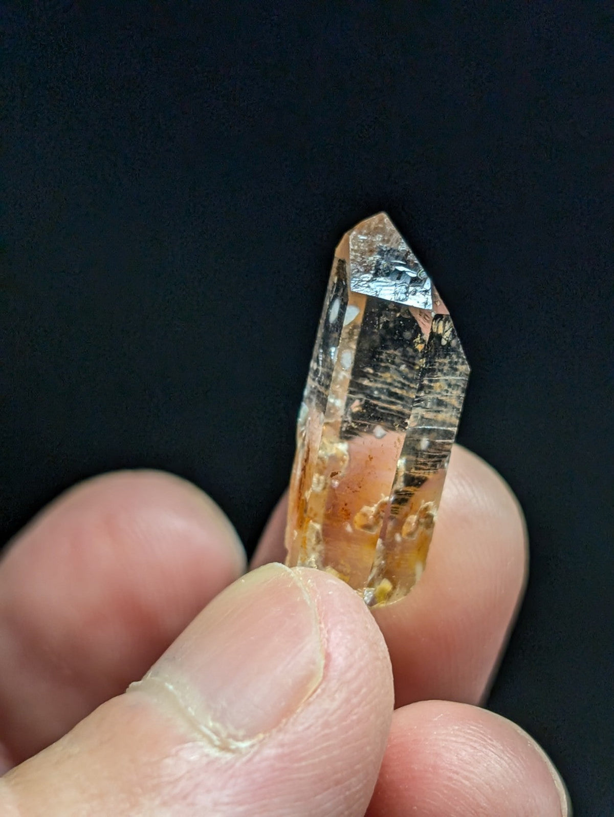 A translucent orange crystal with natural inclusions and a pointed, faceted tip.
