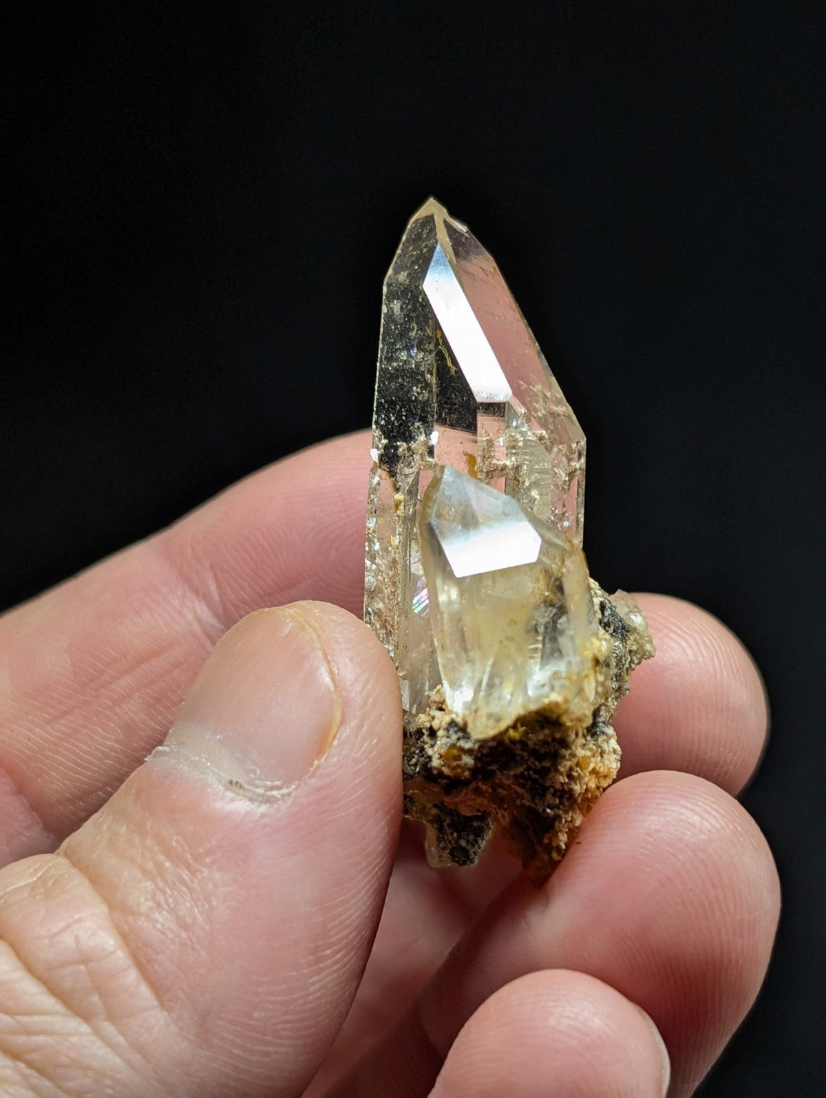 A translucent, pale yellow quartz crystal with a pointed tip and embedded mineral matrix.