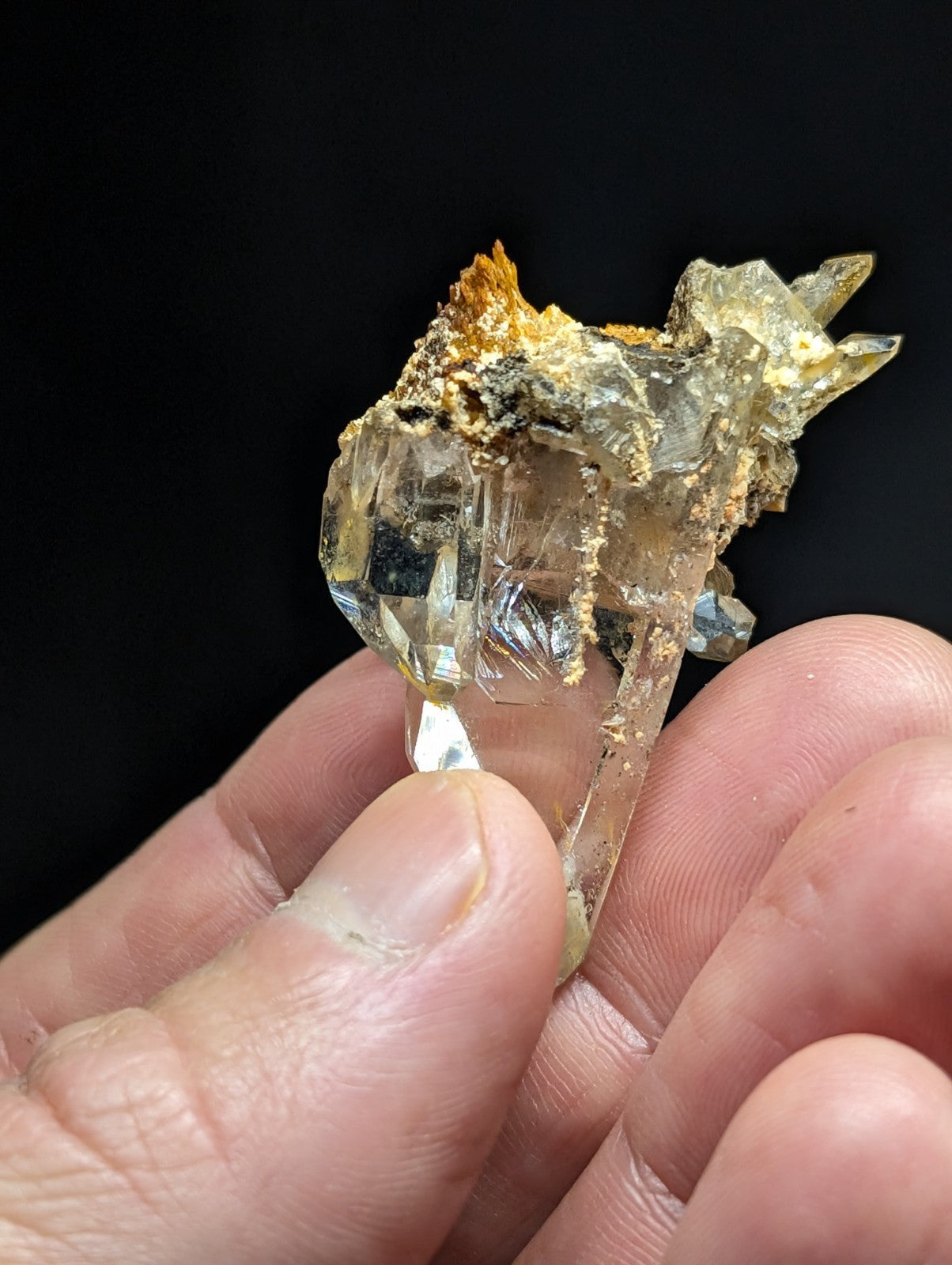 A translucent, crystalline mineral specimen with sharp facets and a mix of clear and golden-yellow hues, held delicately between fingers.