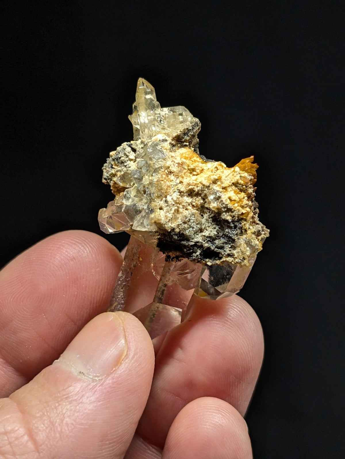 A translucent quartz crystal cluster with golden and dark mineral inclusions, held delicately between fingers.